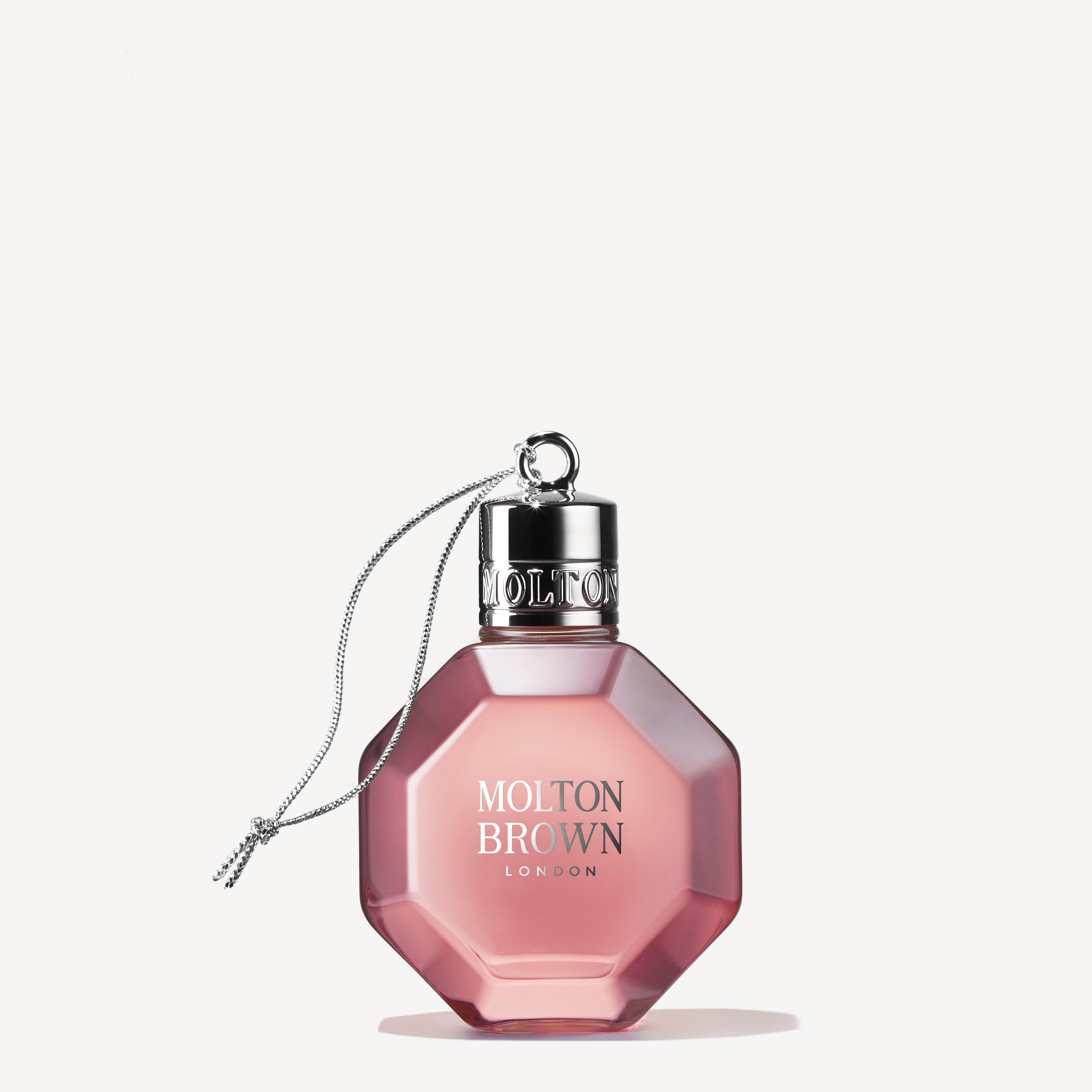 A pink, octagonal perfume bottle featuring a silver cap with an attached chain resembles the Delicious Rhubarb & Rose Festive Bauble. The label displays "MoltonBrown Cyprus" in white lettering. The soft off-white background accentuates the elegant design of this delightful treasure.