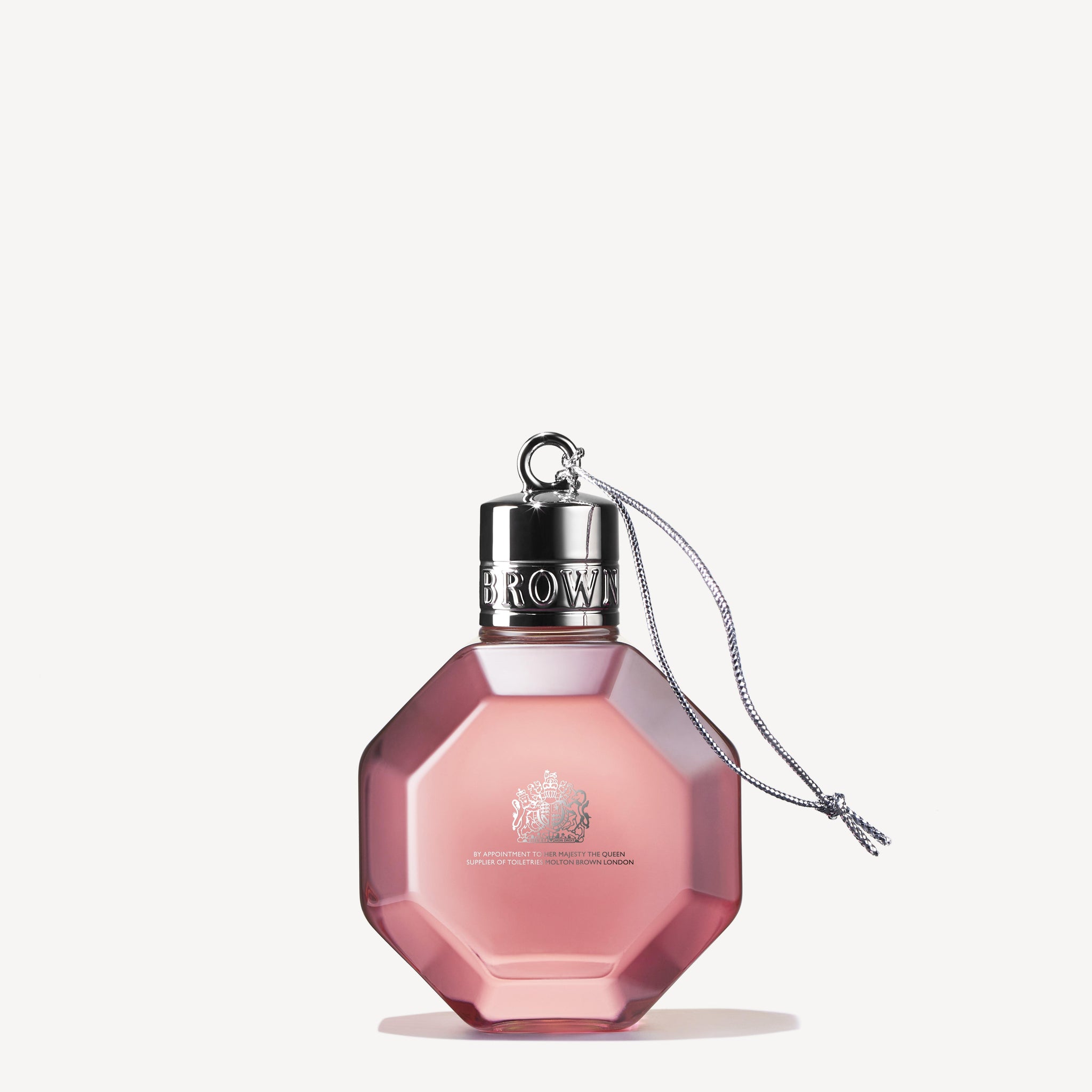 A pink, octagonal "Delicious Rhubarb & Rose Festive Bauble" perfume bottle by MoltonBrown Cyprus features a festive bauble-like charm and a shiny silver cap. The small chain attached complements its etched design and elegant lettering on the front, all set against a plain off-white background.