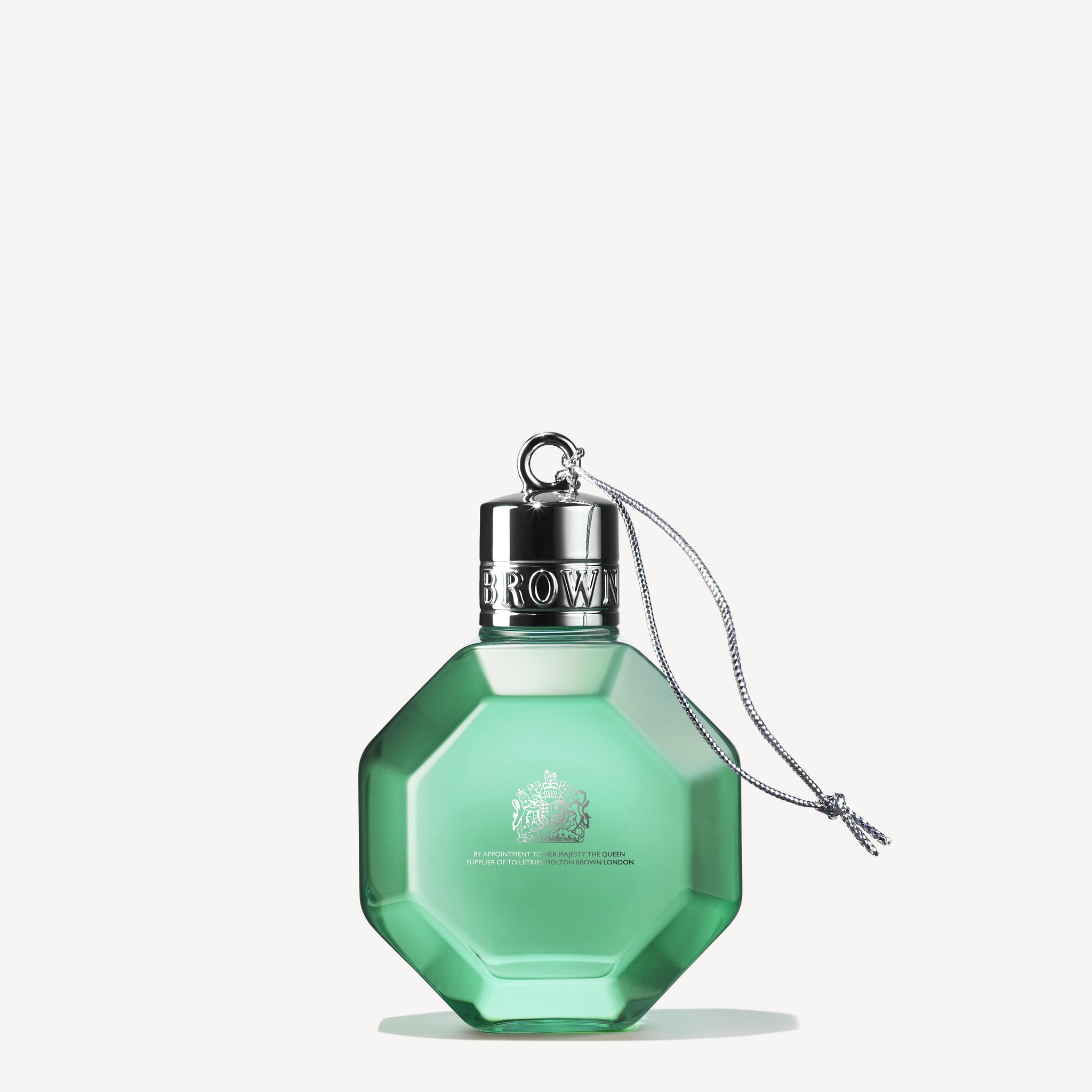 Presenting the Wild Mint & Lavandin Festive Bauble by MoltonBrown Cyprus: a geometric perfume bottle in mint-green, infused with wild mint. This bottle features a sleek silver cap and a sophisticated gray string, with an intricately etched logo. It is elegantly showcased against a light background.