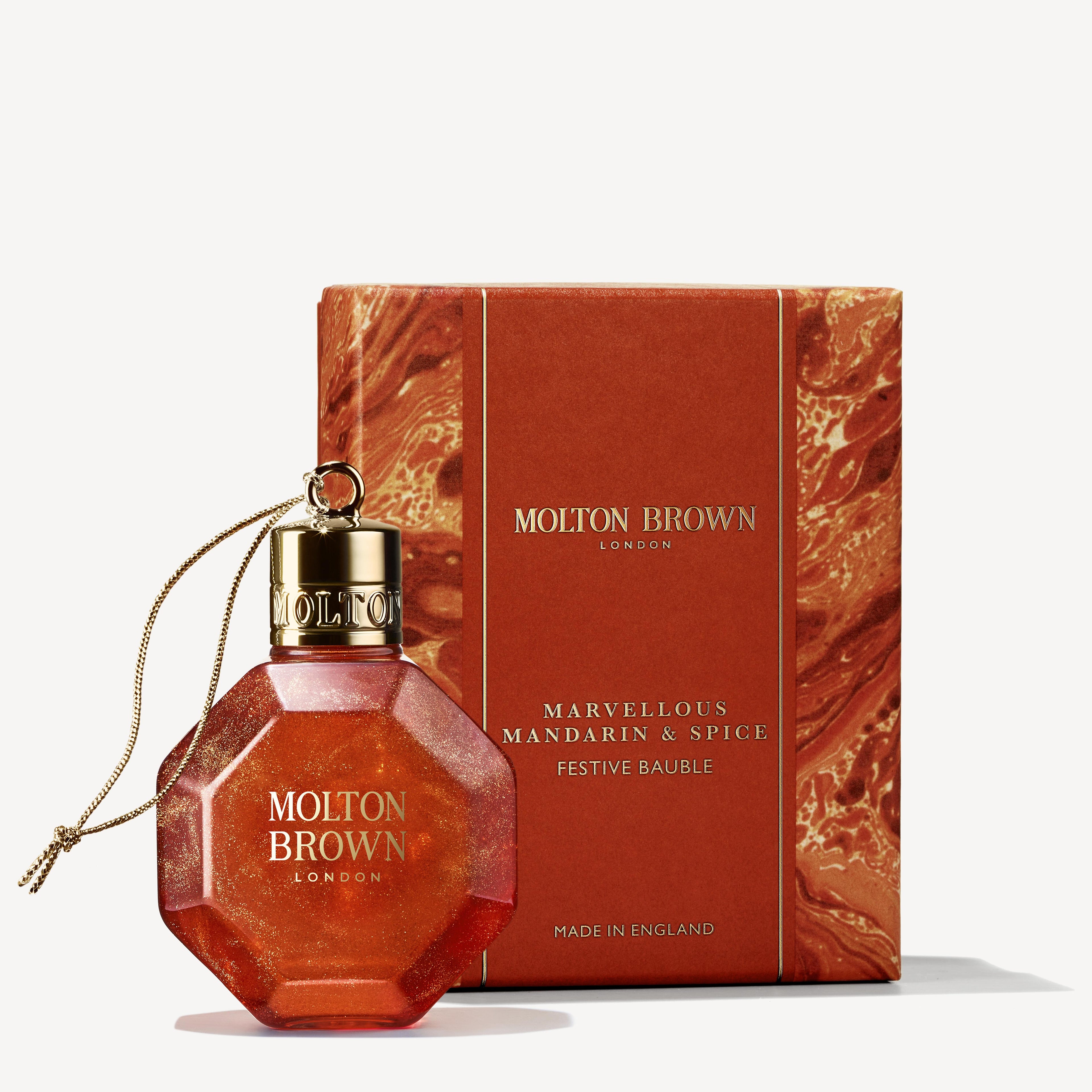 A MoltonBrown Cyprus festive bauble and its packaging. The bauble is orange with a gold cap and string, both labeled MoltonBrown Cyprus, containing a winter citrus body wash. The box mirrors the theme in orange hues, marked as Marvellous Mandarin & Spice Festive Bauble.