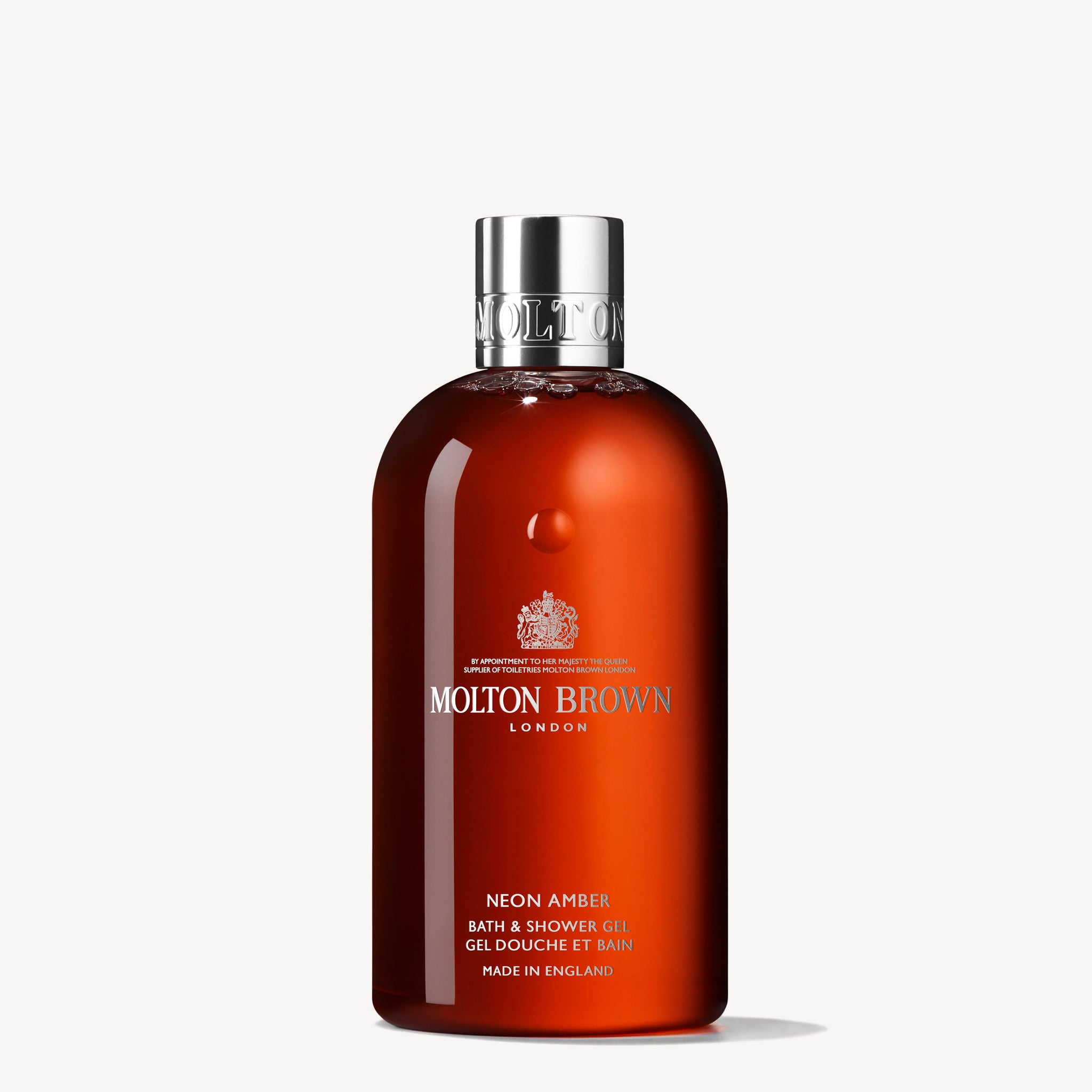 A bottle of Neon Amber Bath & Shower Gel 300ml, infused with refreshing Mandarin Oil, comes in a rich amber container accented by a sleek silver cap. The MoltonBrown Cyprus product prominently displays "Neon Amber" and includes brand details alongside a declaration of its English origin.