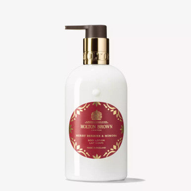 A white bottle of MoltonBrown Cyprus's Merry Berries & Mimosa Body Lotion with a pump dispenser is a luxurious treat for winter skin. The red label featuring gold text and design elements highlights its floral-fruity scent, capturing the essence of red berries.