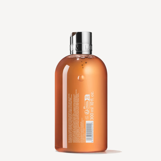 A clear bottle holds the amber-colored Sunlit Clementine & Vetiver Bath & Shower Gel, complete with a silver cap. The label from MoltonBrown Cyprus is reminiscent of a citrus body wash, featuring text and symbols against a light background, indicating a volume of 300 ml (10.1 oz).