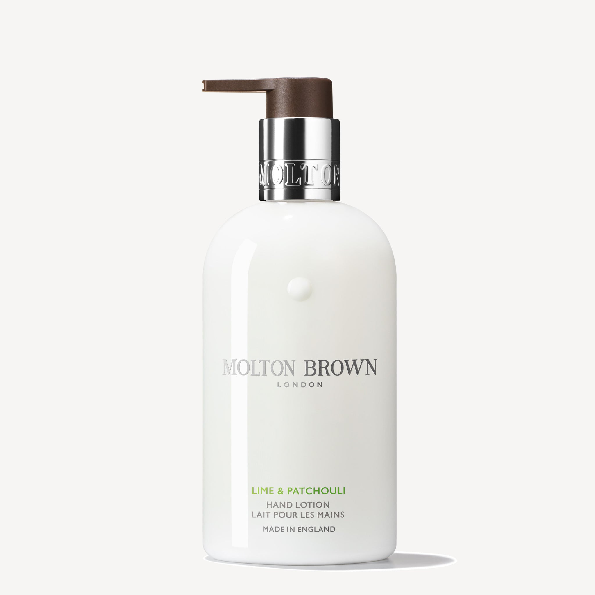 A 300ml bottle of MoltonBrown Cyprus Lime & Patchouli Hand Lotion, complete with a pump dispenser. The packaging is white with a silver and brown cap and showcases elegant branding. Infused with makrut lime leaves, this lotion exudes luxury and bears the "Made in England" mark at the bottom.