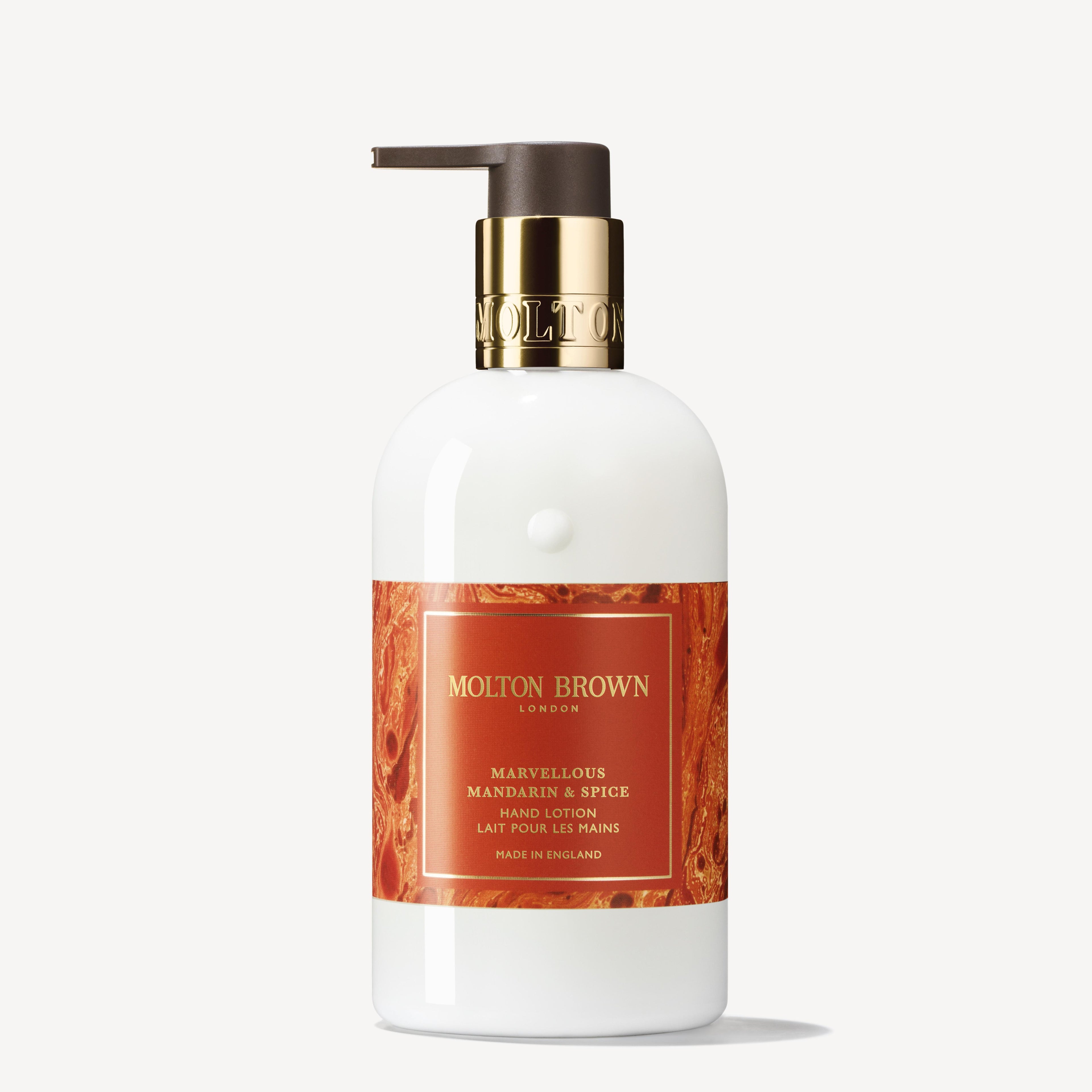 A MoltonBrown Cyprus hand lotion bottle featuring a convenient pump showcases the Marvellous Mandarin & Spice label against a warm, textured orange backdrop. Infused with subtle notes of cinnamon, the elegant metallic cap is adorned with MoltonBrown branding.