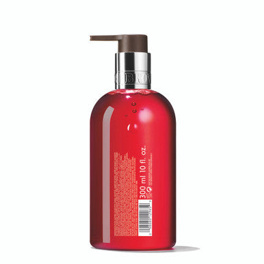 A red bottle of Festive Frankincense & Allspice Fine Liquid Hand Wash from MoltonBrown Cyprus, featuring a brown pump dispenser and labeled with product details. The woody hand wash indicates 300 ml and 10 fl. oz. on the front, along with a barcode and small text on the back.