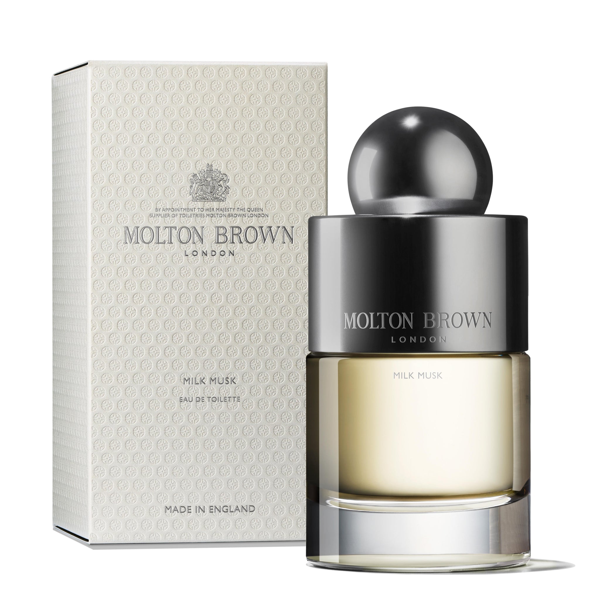 Beside the embossed white packaging of MoltonBrown Cyprus, a Milk Musk Eau de Toilette 100ml bottle is showcased. It boasts a sleek design with a metallic cap and label, emanating an opulent floral-musky fragrance enriched by the depth of Ambroxan.