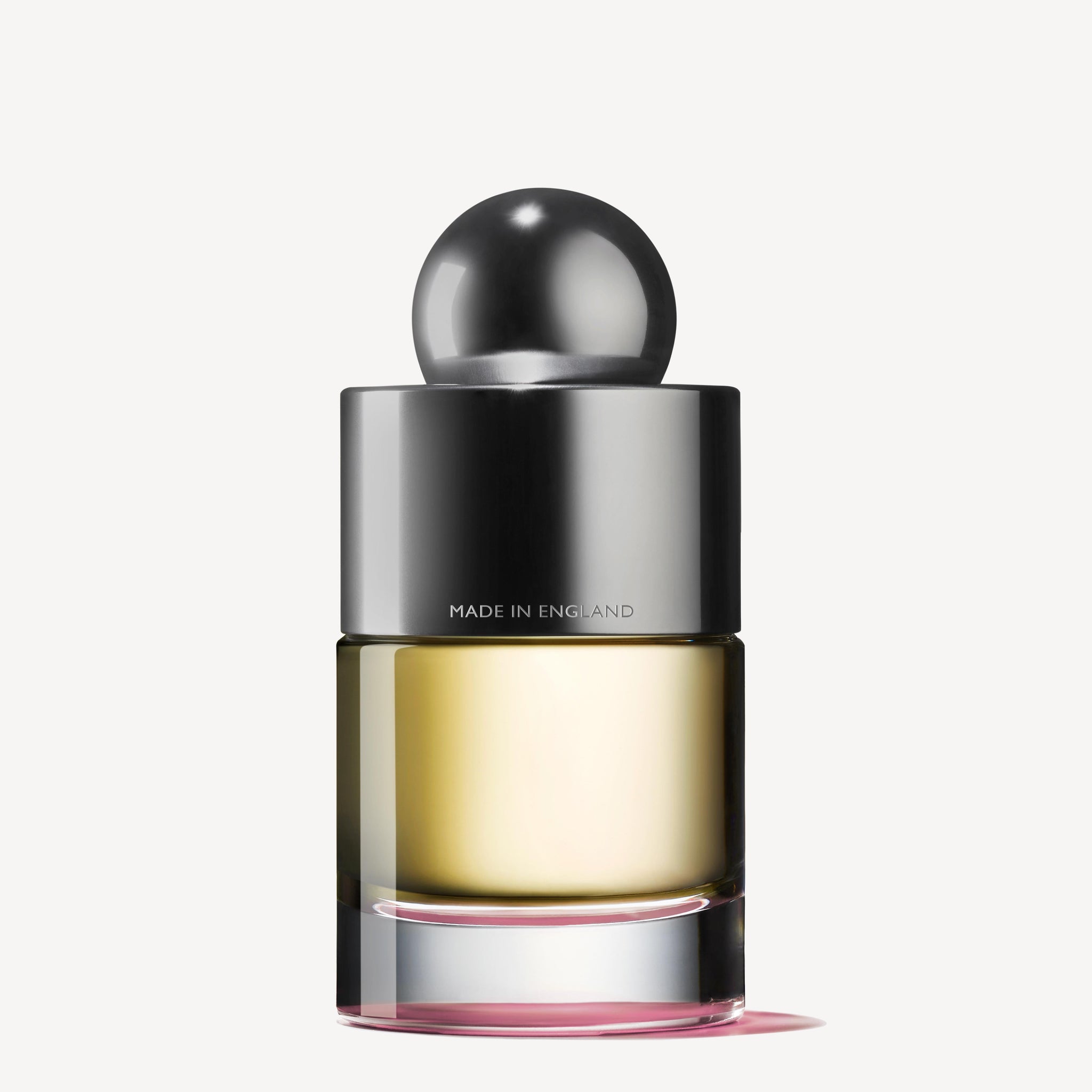 The Rose Dunes Eau de Toilette 100ml by Molton Brown Cyprus features a sleek metallic cap and round top. This Made in England perfume bottle holds a pale yellow fragrance laced with cassis notes, elegantly showcased against a simple, light background.