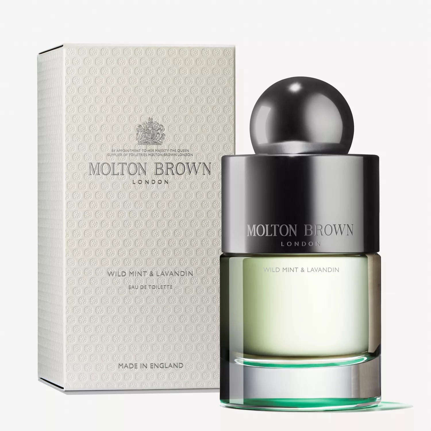 The MoltonBrown Cyprus Wild Mint & Lavandin Eau de Toilette 100ml is elegantly displayed beside its packaging, featuring a clear bottle with a glossy black cap alongside a subtly patterned, light-colored box that hints at the fresh wild mint aroma within.