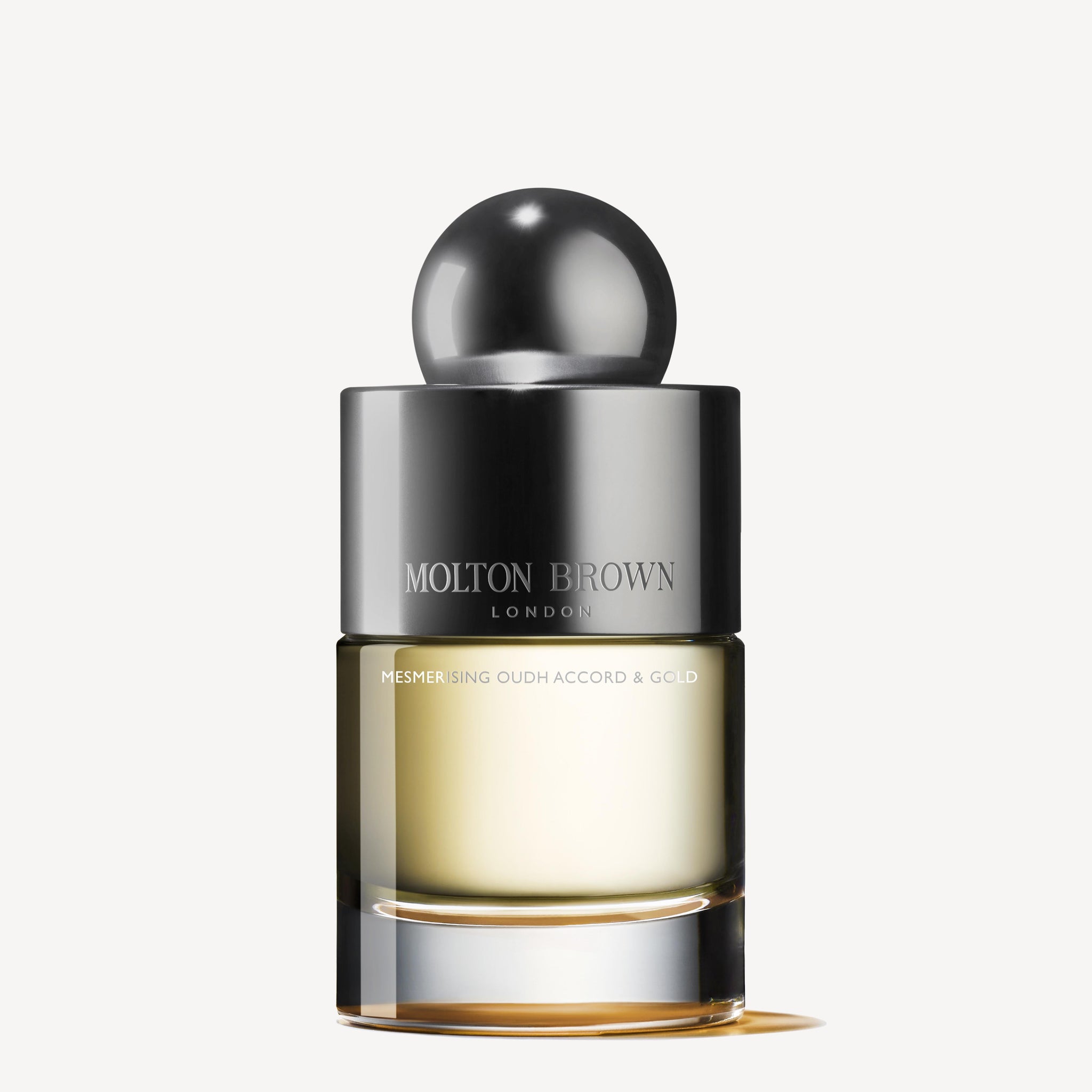A bottle of MoltonBrown Cyprus Mesmerising Oudh Accord & Gold Eau de Toilette 100ml, adorned with a sleek, reflective silver cap and filled with a gradient of light yellow liquid. The design is modern and elegant, perfectly capturing the essence of Eau de Toilette.