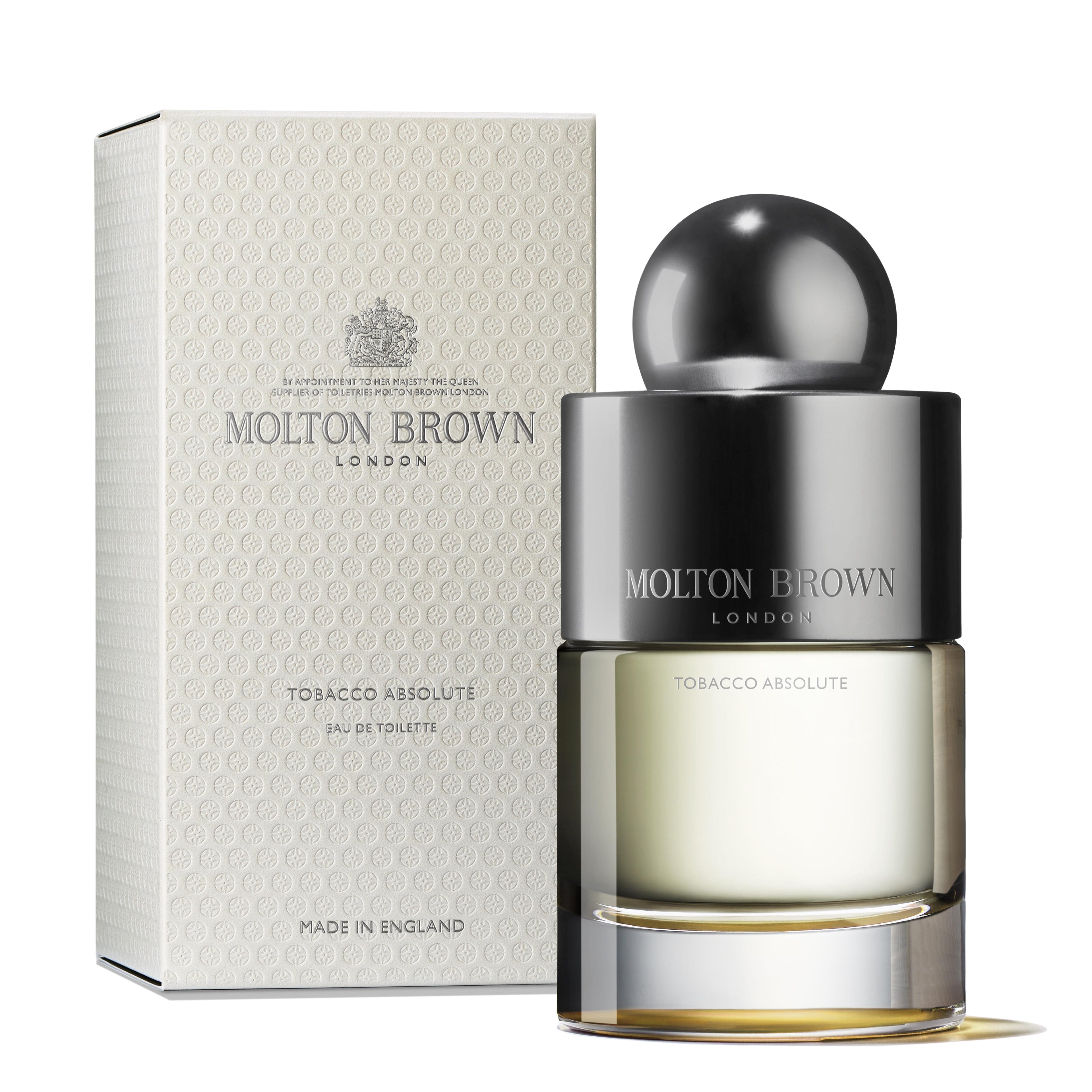 A 100ml glass bottle of MoltonBrown Cyprus' Tobacco Absolute Eau de Toilette, topped with a spherical cap, sits next to its textured, cream-colored box. This woody fragrance highlights notes of tobacco and grapefruit. Both the bottle and the box proudly display "Made in England," showcasing an air of sophistication.