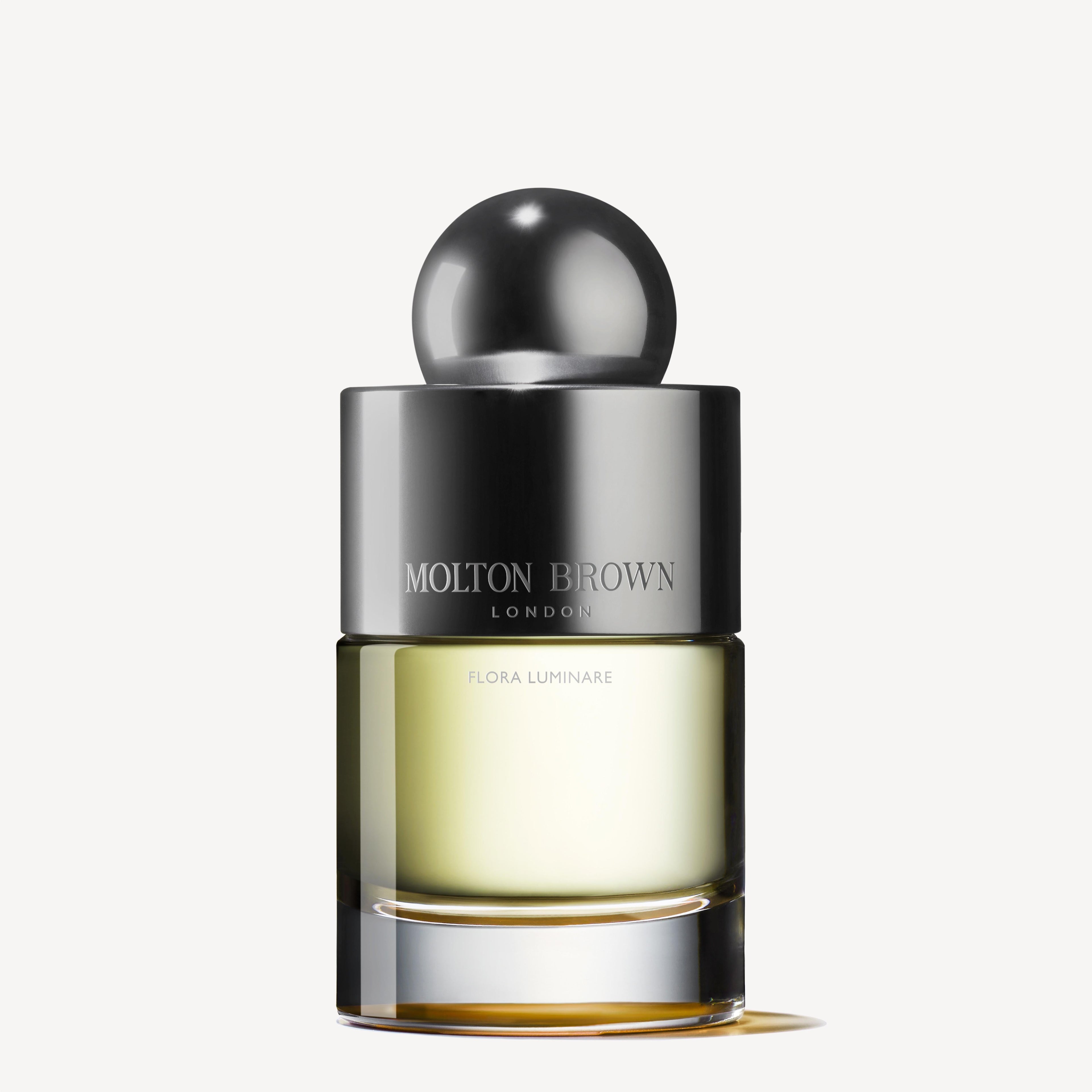 A bottle of Flora Luminare Eau de Toilette 100ml by Molton Brown Cyprus features a sleek, rounded metallic cap. Adorned with the brand name and fragrance type on the label, it is half-filled with a light yellow liquid, offering whispers of Polynesian frangipani for an exotic olfactory escape.