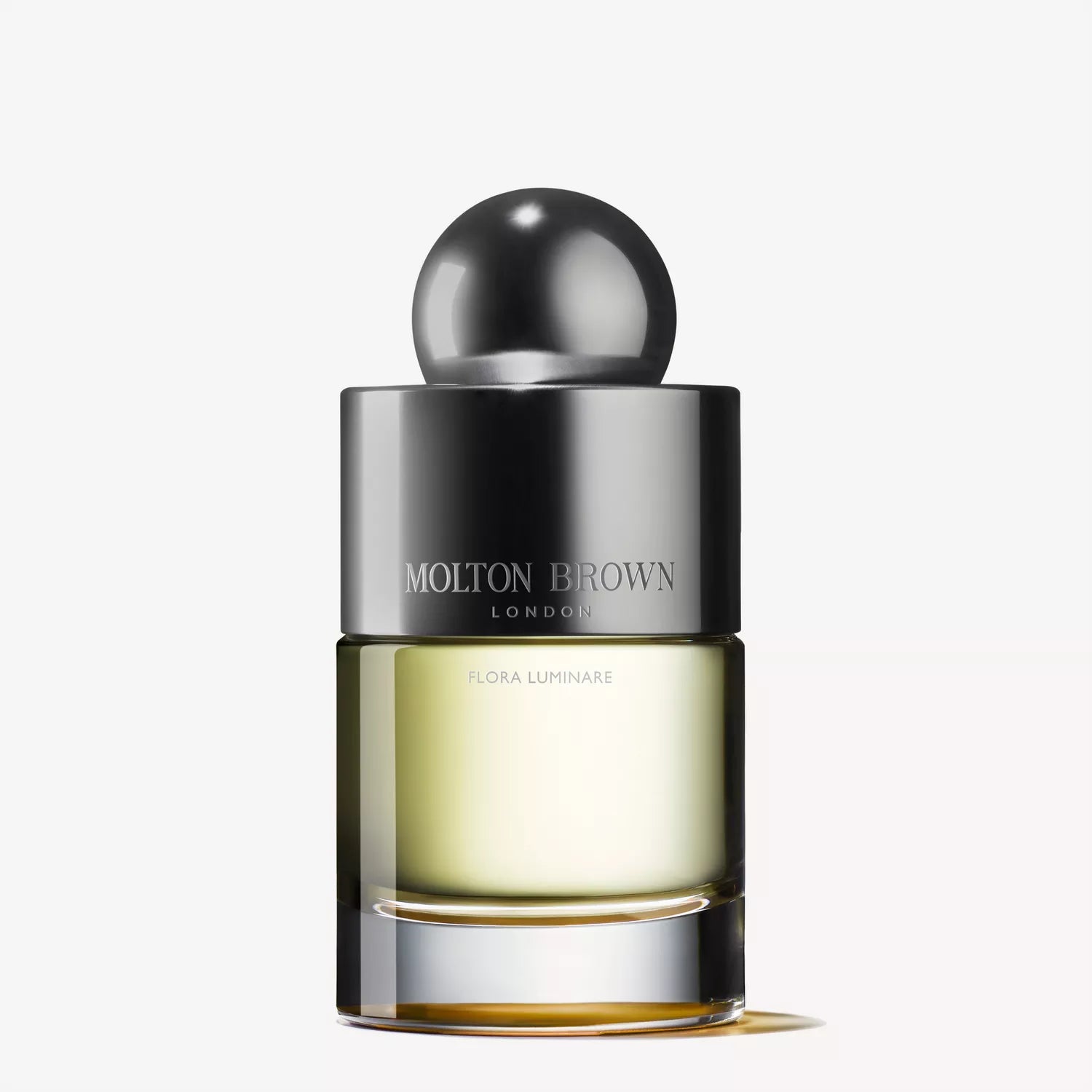 The Flora Luminare Eau de Toilette by Molton Brown Cyprus features a sleek perfume bottle with a round silver cap and light yellow liquid that exudes Polynesian frangipani. Its minimalist design, set against a plain white background, captures subtle elegance.