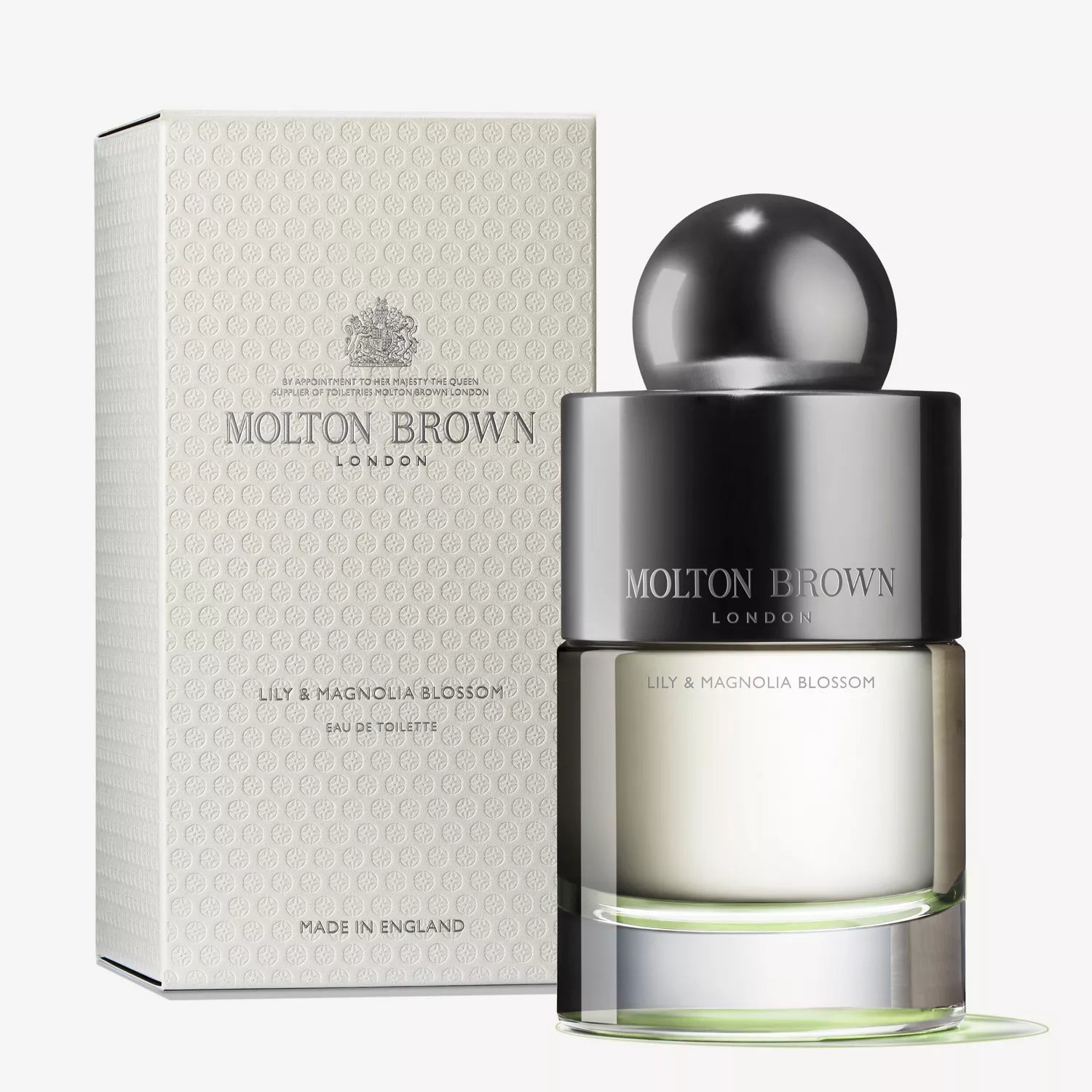 A Molton Brown Cyprus perfume bottle, Lily & Magnolia Blossom Eau de Toilette 100ml, stands elegantly before its matching white box. The bottle features a round black cap and an elegant design, offering a captivating floral fragrance, while the box displays the brands logo and details.