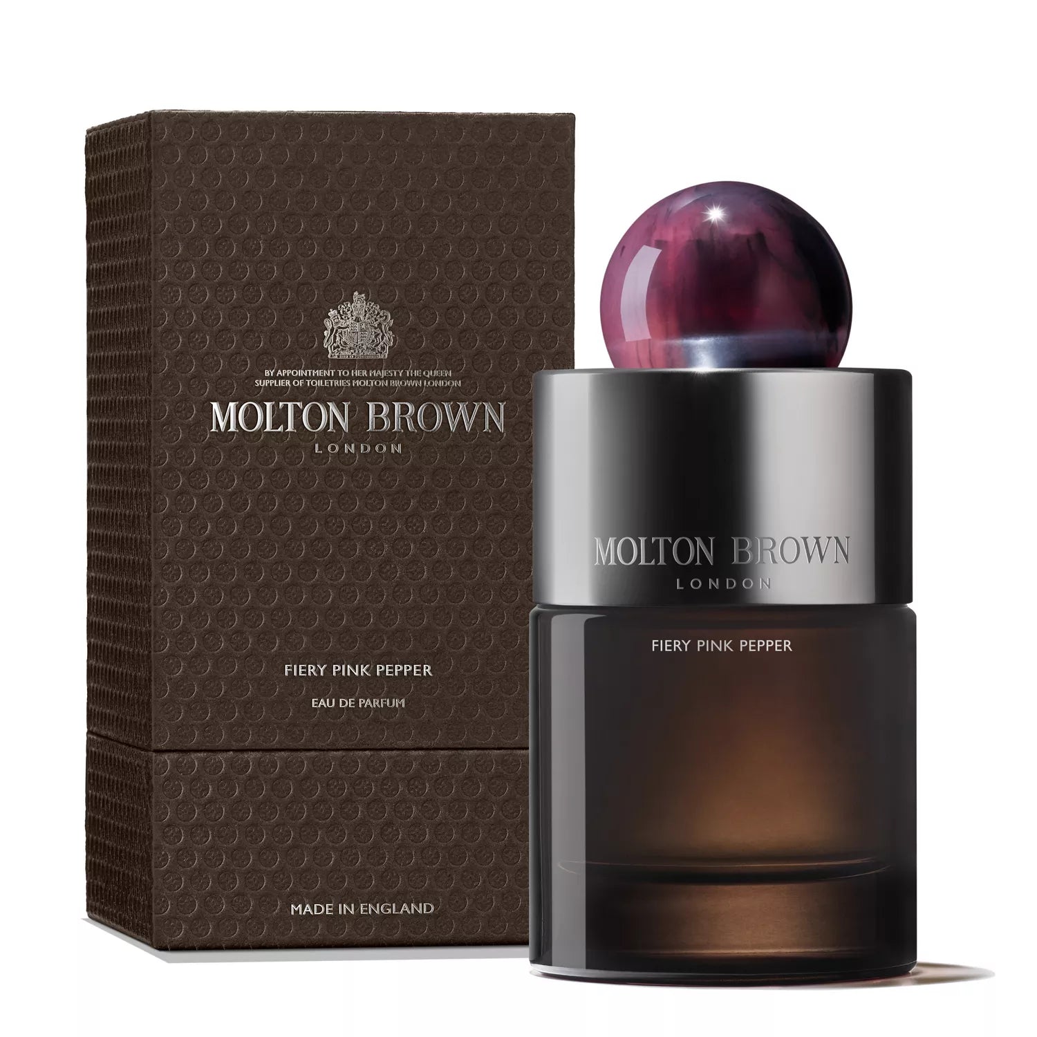 A dark, cylindrical bottle of MoltonBrown Cyprus Fiery Pink Pepper Eau de Parfum 100ml is displayed with its box. It has a pink and purple spherical cap, while the textured box with a repeating pattern enhances this spicy pink pepper fragrances stylish design.