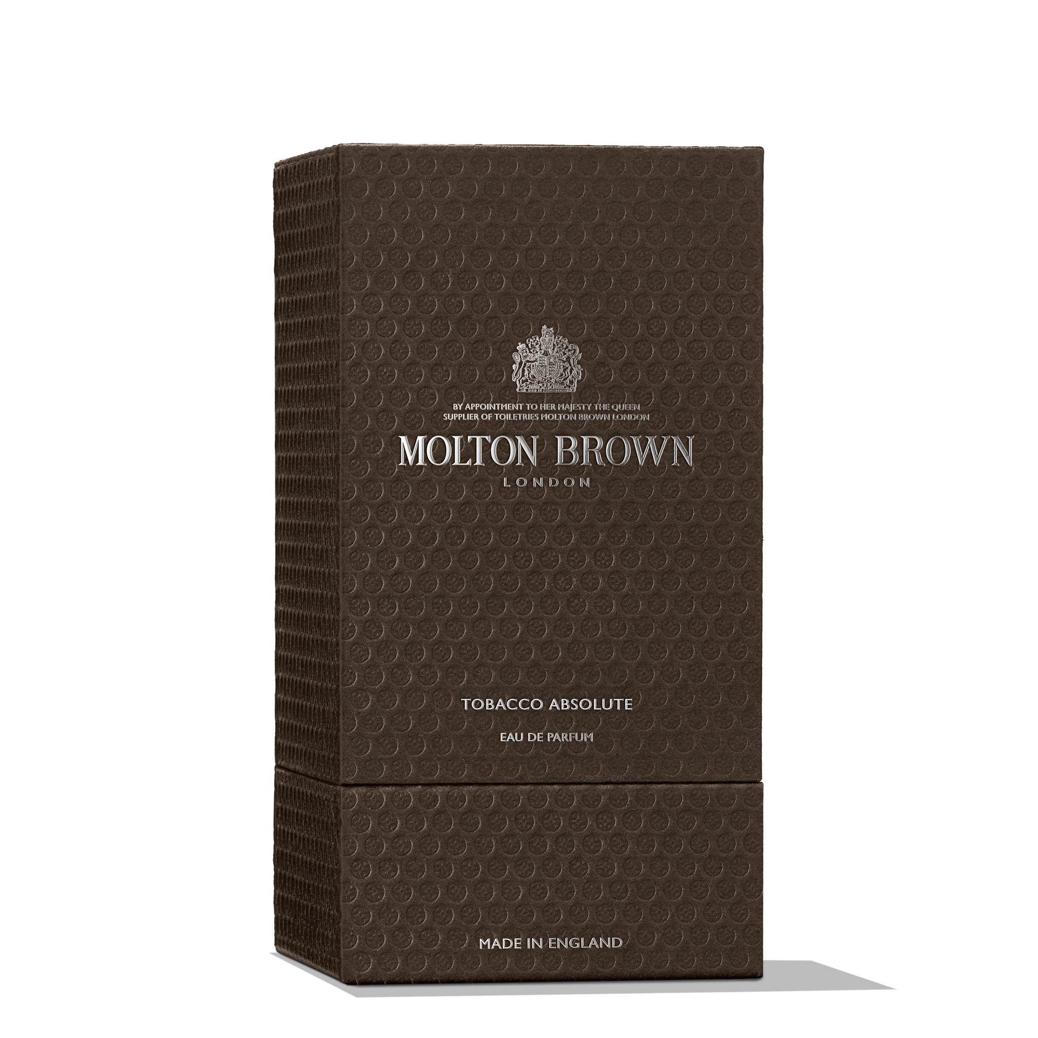 A dark brown textured box featuring the MoltonBrown Cyprus logo in silver text is labeled Tobacco Absolute Eau de Parfum 100ml. Produced in England, it encapsulates a smoky tobacco scent with a woody fragrance. The packaging is enhanced with a subtle circular pattern.