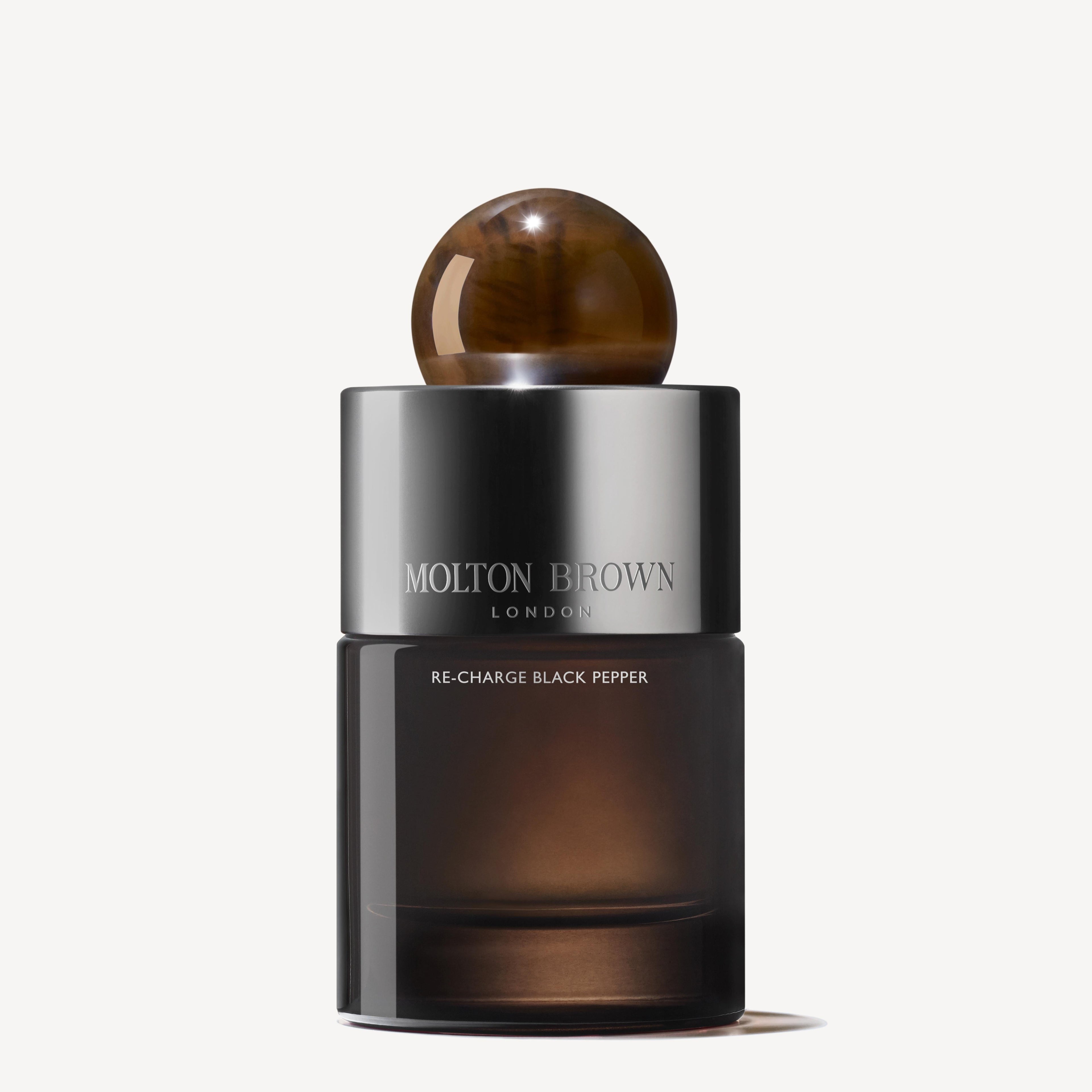 A sophisticated Re-charge Black Pepper Eau de Parfum 100ml from MoltonBrown Cyprus is nestled against a plain white background. This elegant bottle boasts a round brown cap and a gradient black and silver design, offering tantalizing hints of bergamot to spark curiosity.