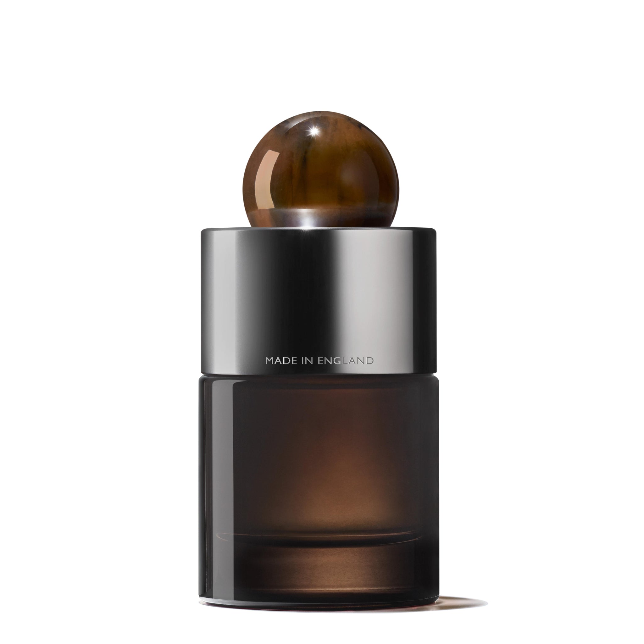 The Re-charge Black Pepper Eau de Parfum from Molton Brown Cyprus comes in a sleek bottle featuring a cylindrical black body with a metallic silver cap, topped with an amber-like round stopper. The words "Made in England" are elegantly engraved on the silver portion. This exquisite presentation is set against a plain white background.