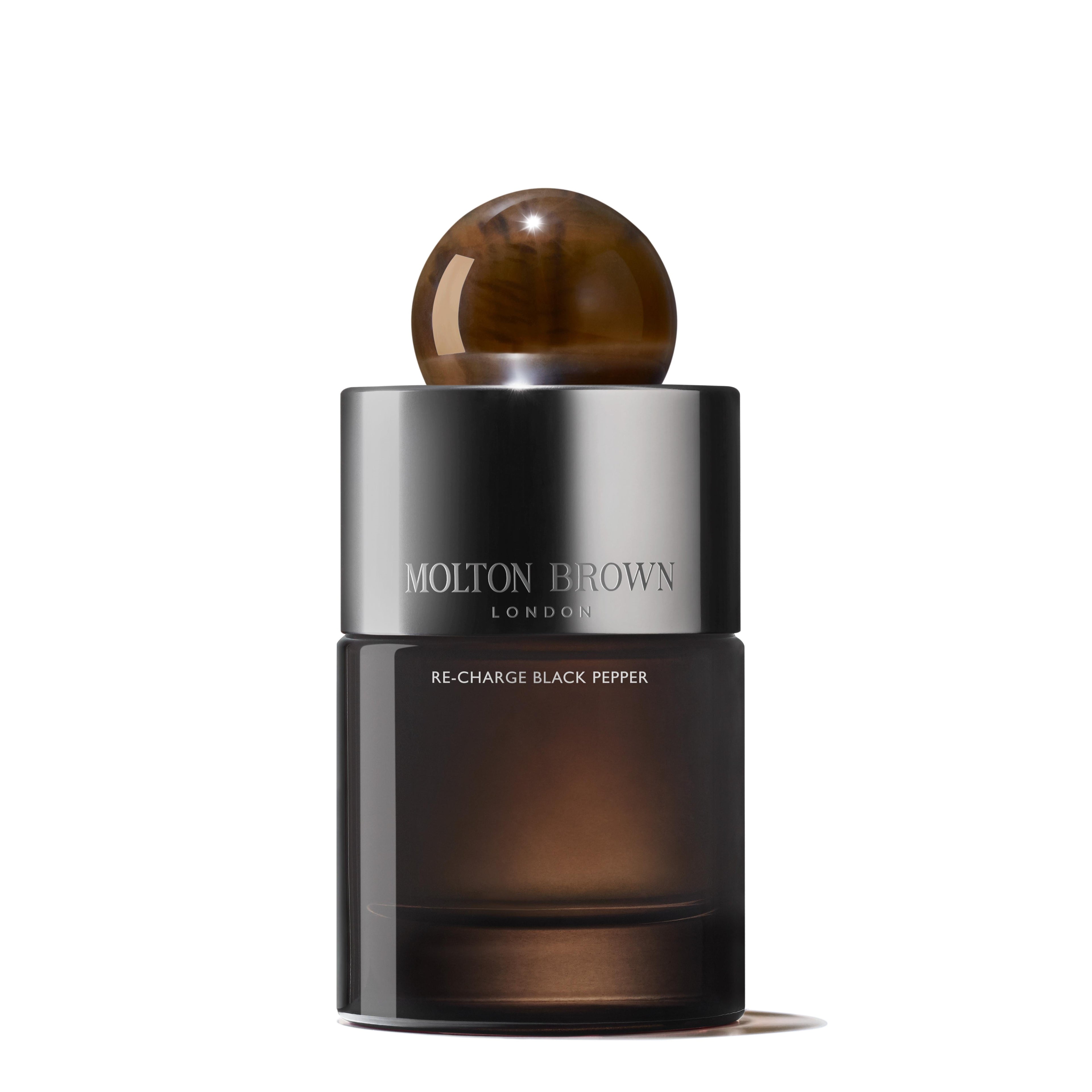 The Re-charge Black Pepper Eau de Parfum 100ml by MoltonBrown Cyprus is presented in a cylindrical bottle with a dark gradient design and a round, brown cap. The metallic silver label elegantly displays the brand and product name. Aromatic notes of bergamot and vetiver add to its enticing fragrance.