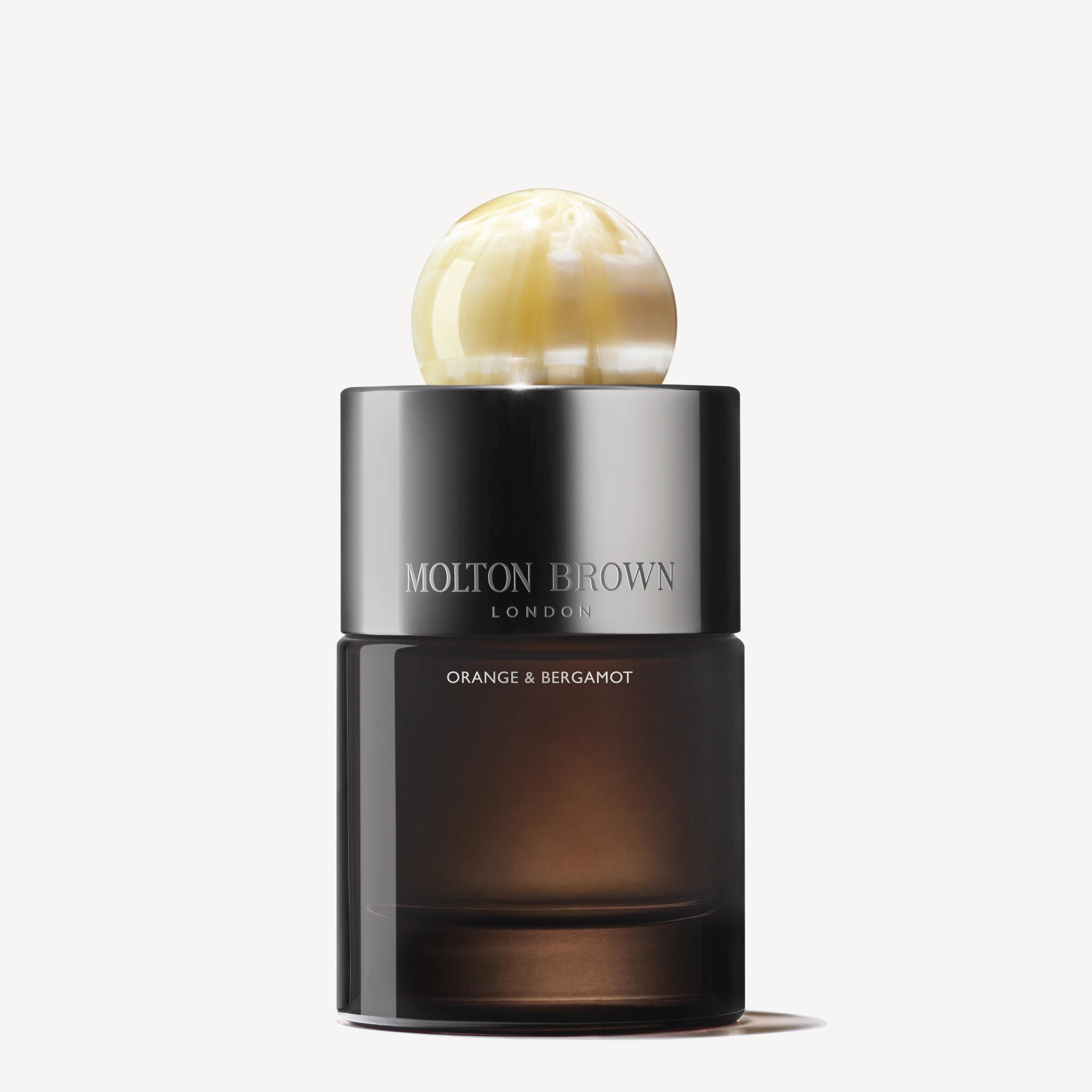 A black, cylinder-shaped bottle of MoltonBrown Cyprus Orange & Bergamot Eau de Parfum 100ml is displayed against a white background, featuring a creamy and light yellow marble-like round cap. The fragrance captivates with notes of orange flowers and musky woods.