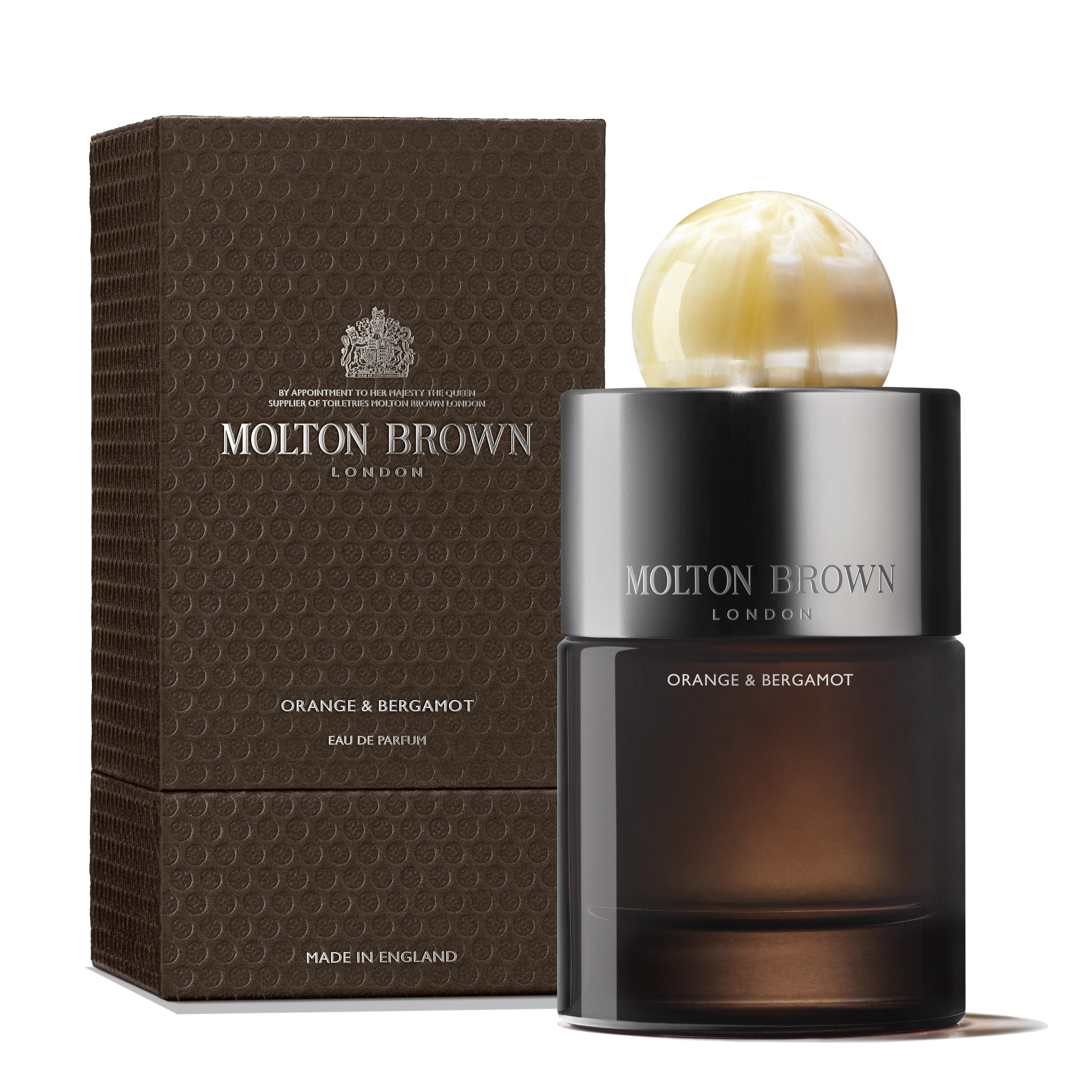 A MoltonBrown Cyprus Orange & Bergamot Eau de Parfum 100ml bottle and box. The bottle is adorned with a round, pearl-like cap and features the brand name alongside the scent "Orange & Bergamot." The textured box displays the same brand and scent text, evoking musky-woods aromas, and is positioned upright next to the bottle.