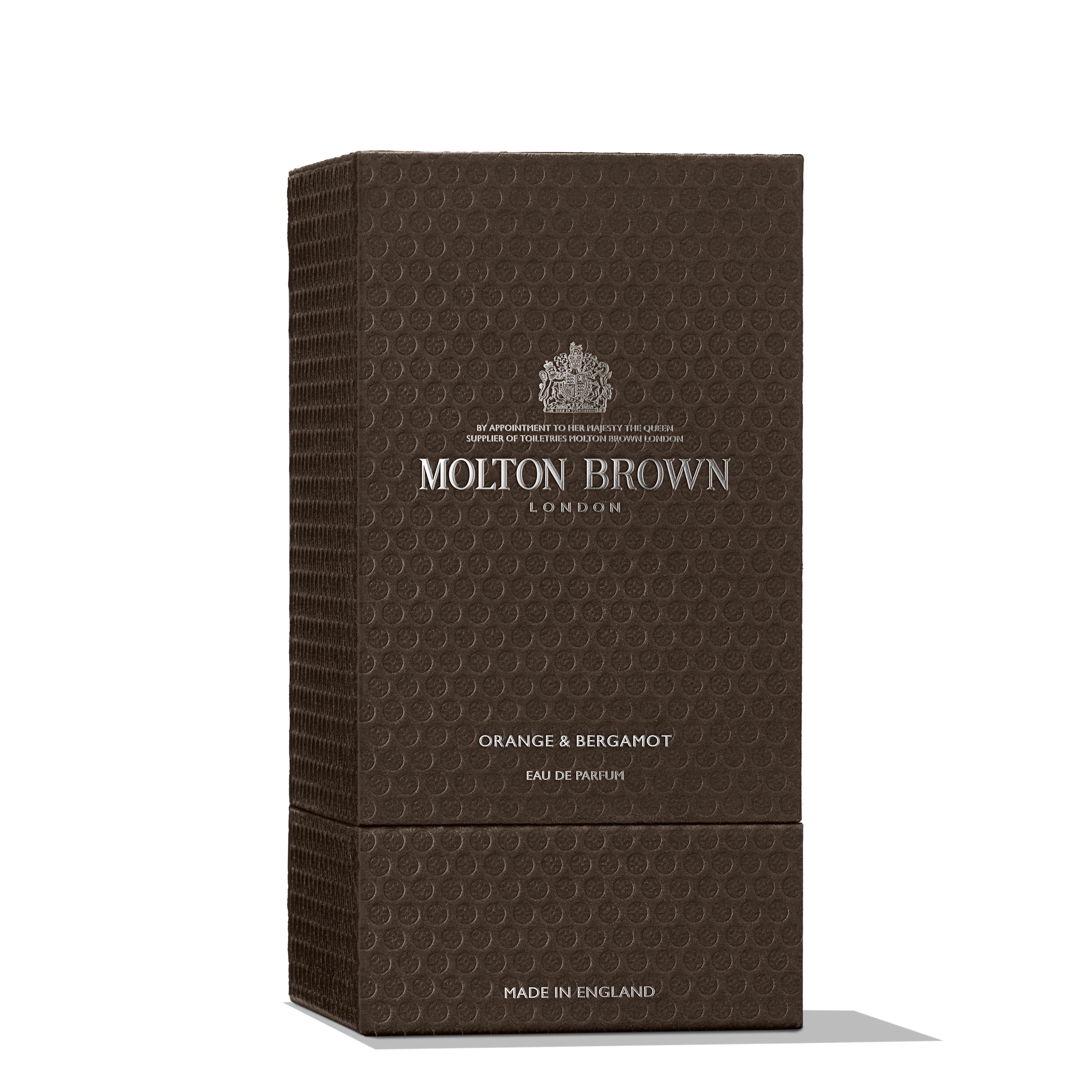 A textured brown box of MoltonBrown Cyprus Orange & Bergamot Eau de Parfum 100ml, featuring silver embossed text and logo, exudes elegance. The box's pattern of small circles hints at the musky-woods scent, with "Made in England" elegantly inscribed at the bottom.