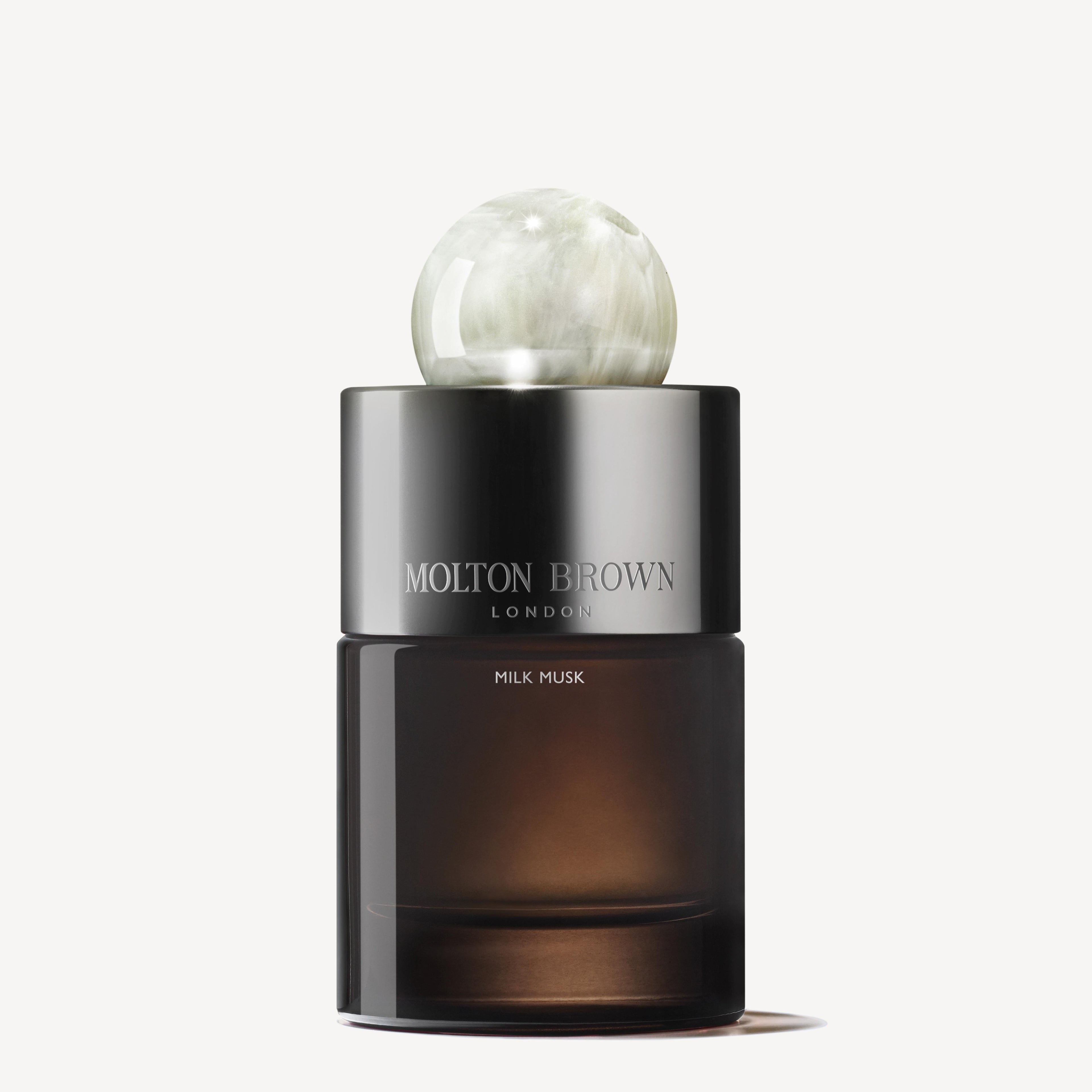 The MoltonBrown Cyprus Milk Musk Eau de Parfum 100ml bottle showcases a dark glass design topped with a round, marble-like cap, embodying a sense of tranquillity. It is elegantly positioned against a plain, light background.