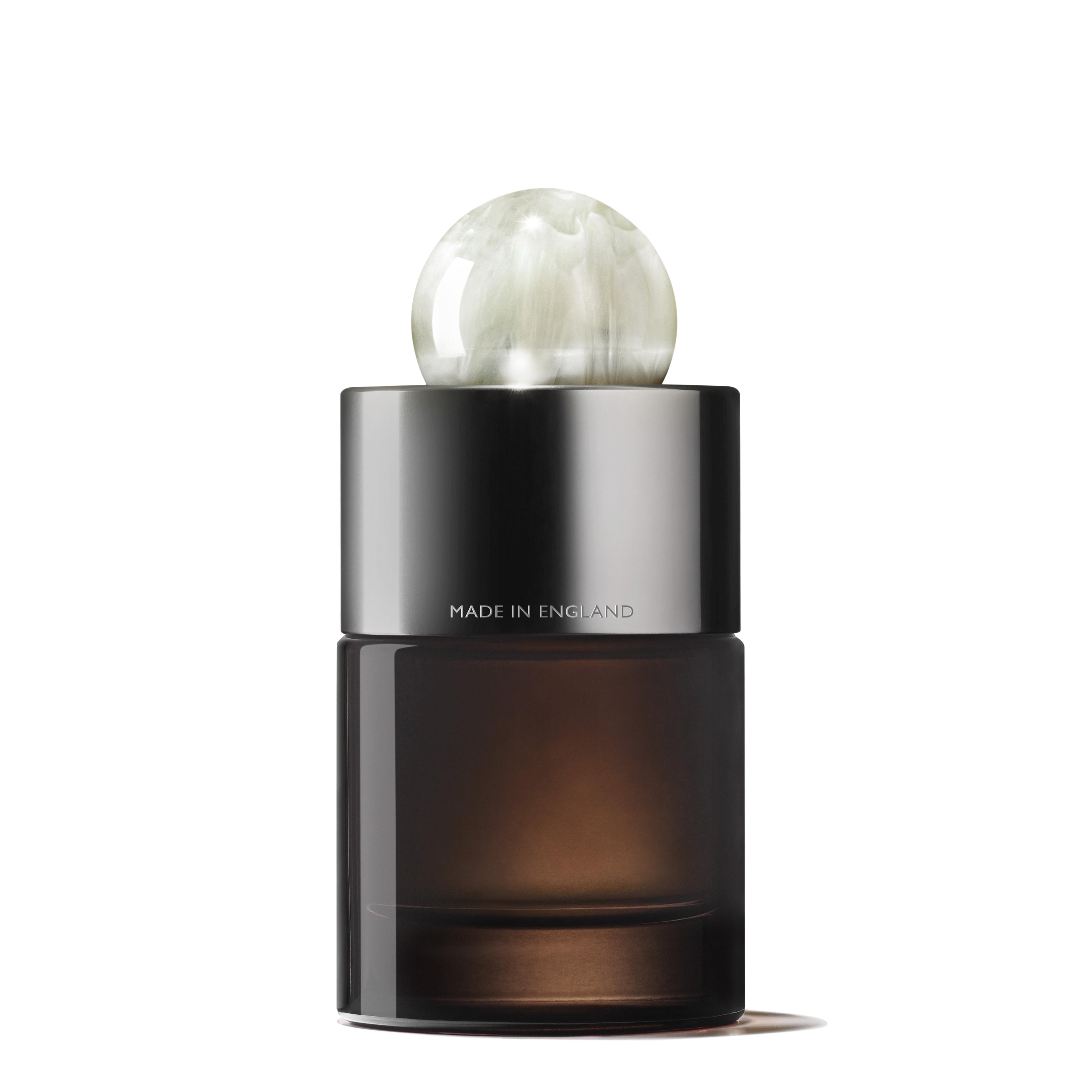 A sleek, cylindrical bottle of Milk Musk Eau de Parfum by MoltonBrown Cyprus features a dark glass base and a metallic cap. The cap is adorned with a decorative, translucent sphere, embodying tranquility. Text on the bottle reads Made in England.