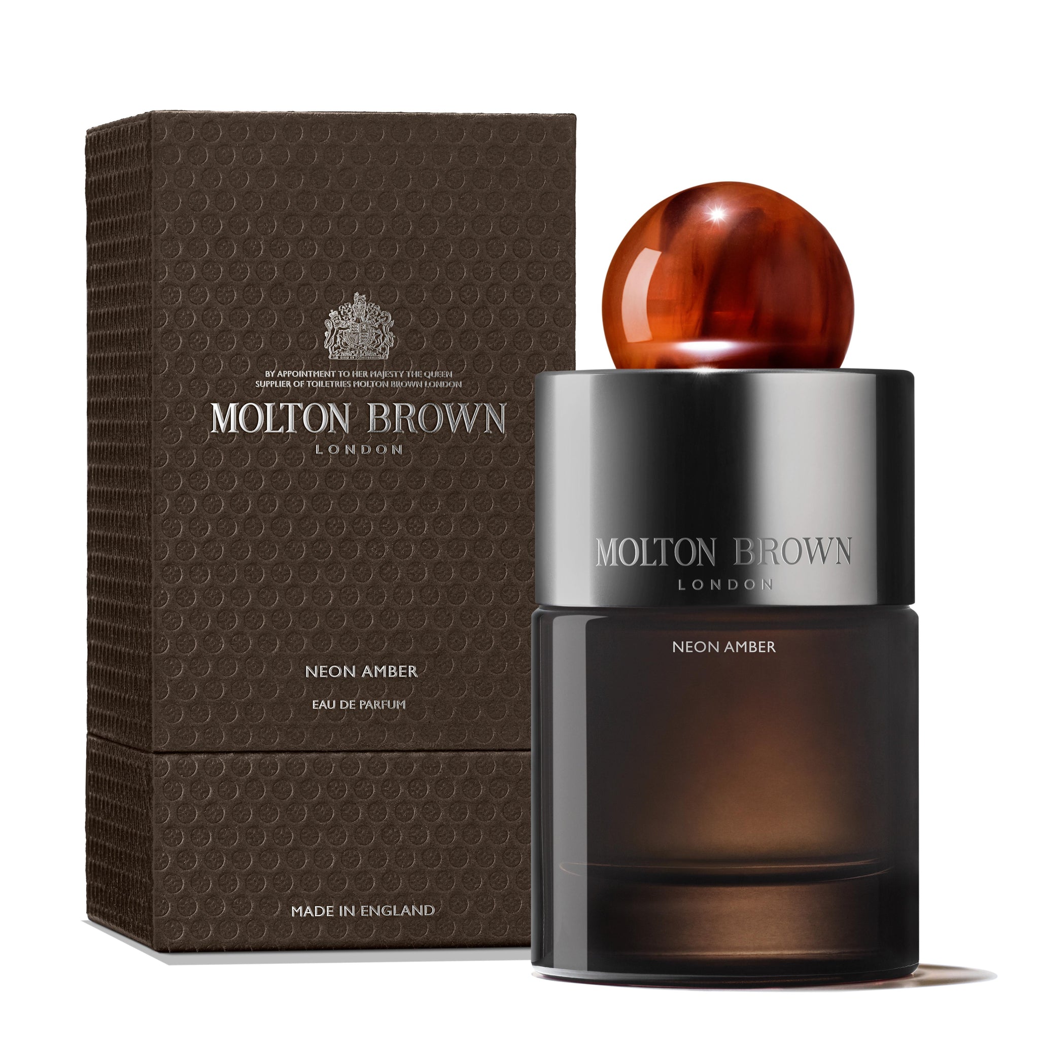 The Neon Amber Eau de Parfum 100ml by Molton Brown Cyprus, crafted by Jérôme Di Marino, features a striking spherical amber cap and is presented in textured brown packaging. The elegant lettering of the brand and fragrance names on both the bottle and box suggests its sophisticated blend of tonka absolute.