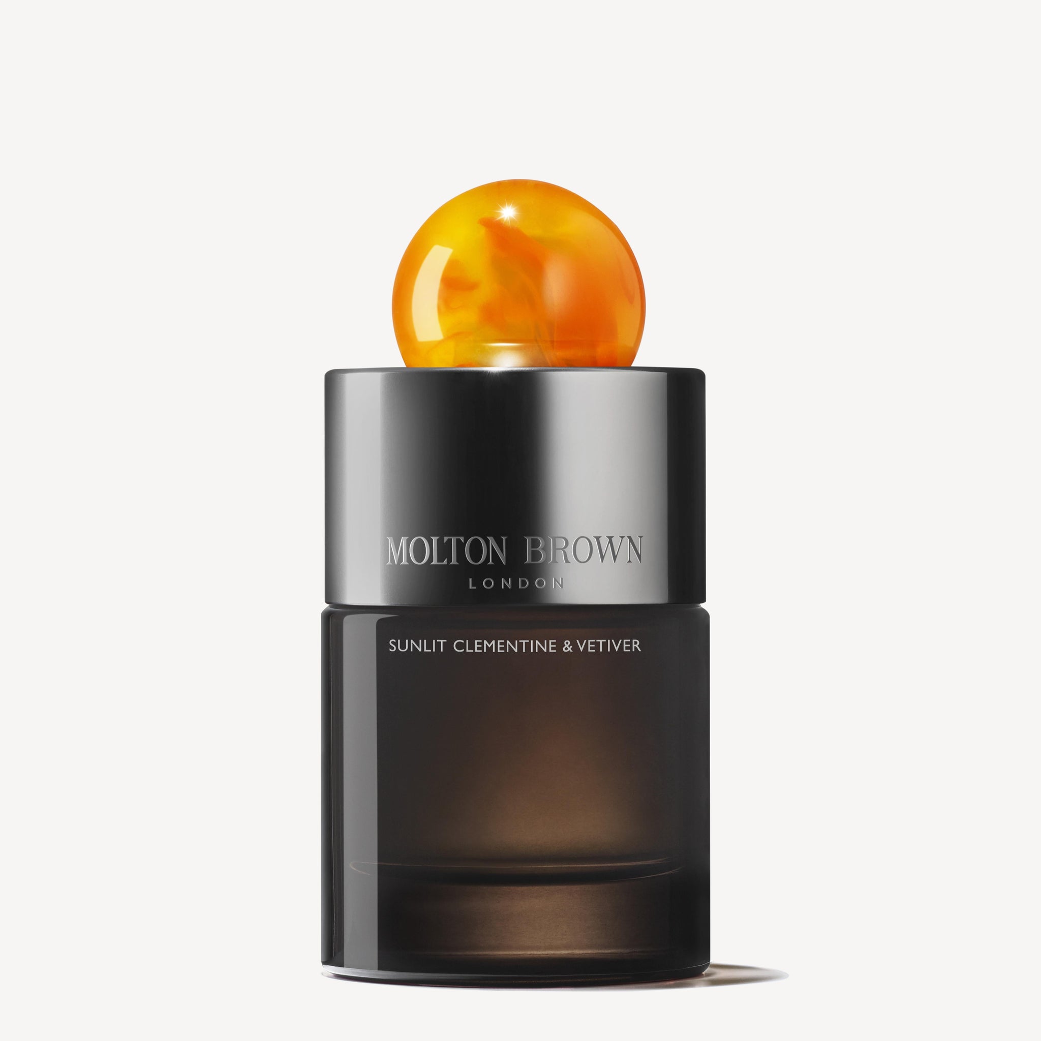 A bottle of MoltonBrown Cyprus Sunlit Clementine & Vetiver Eau de Parfum 100ml is elegantly presented. The sophisticated dark container, topped with a round orange cap, perfectly embodies the zest of clementine and mandarin, capturing the vibrant freshness and rich allure of bourbon vetiver.