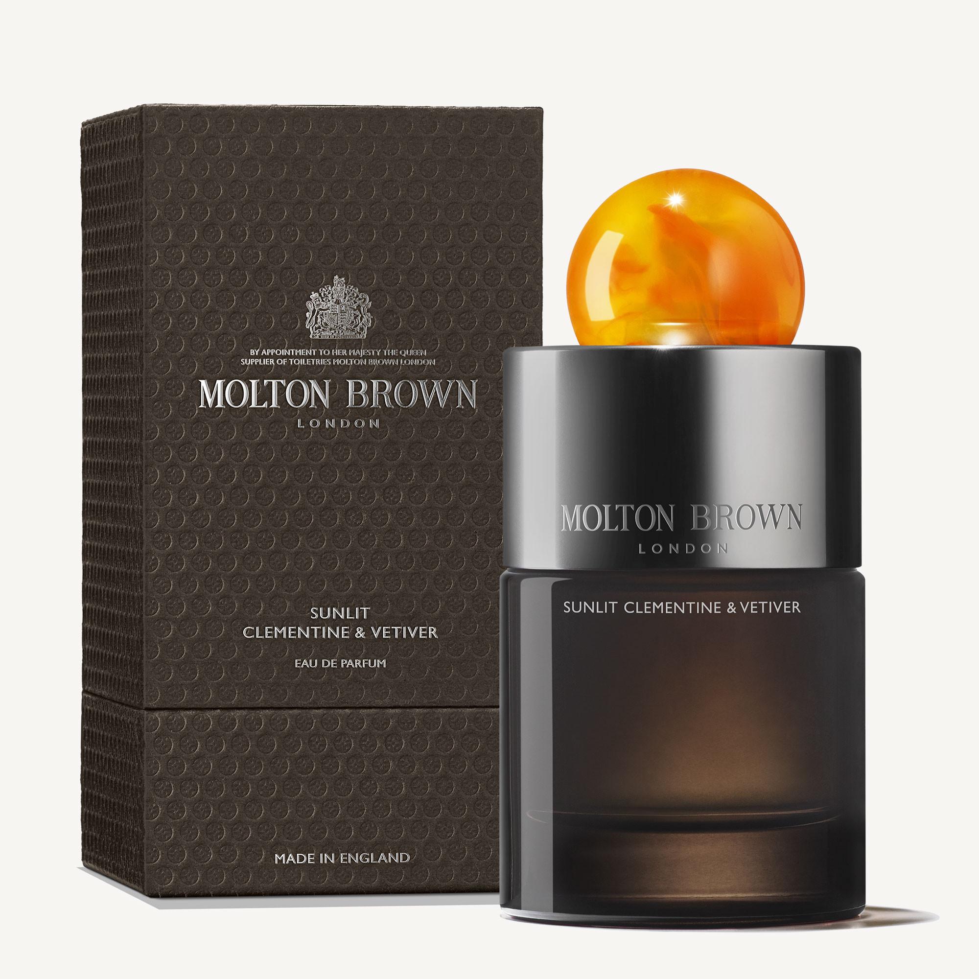 A MoltonBrown Cyprus perfume bottle features an amber spherical cap and is positioned before a textured black box. Both display the text Sunlit Clementine & Vetiver Eau de Parfum 100ml. The packaging radiates an elegant and sophisticated allure.