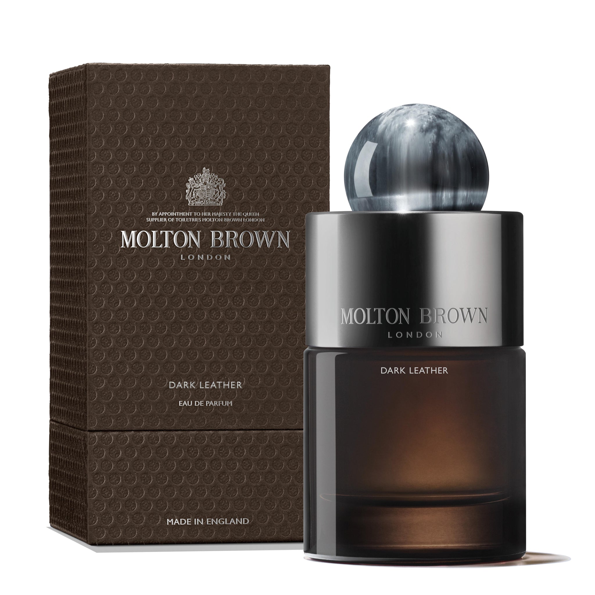 A bottle of MoltonBrown Cyprus Dark Leather Eau de Parfum 100ml, featuring a spherical cap, is placed next to its textured brown box. The fragrance blends smoky leather with crisp lavender notes. The packaging displays the brand and product details.