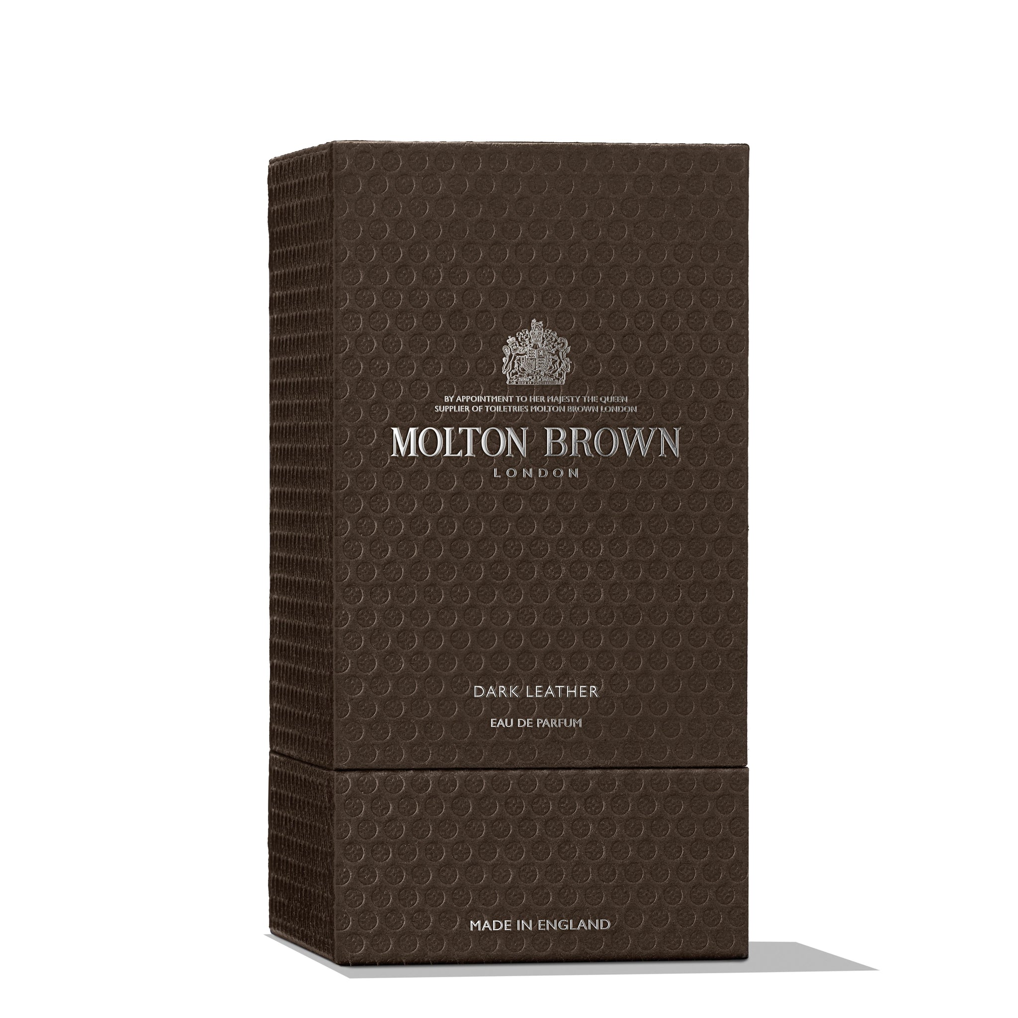 A textured, brown rectangular box of MoltonBrown Cyprus Dark Leather Eau de Parfum 100ml is displayed. Accented with silver lettering, the box highlights its luxury and English origin. The scent within reveals hints of crisp lavender harmonized with smoky leather notes, epitomizing elegance.