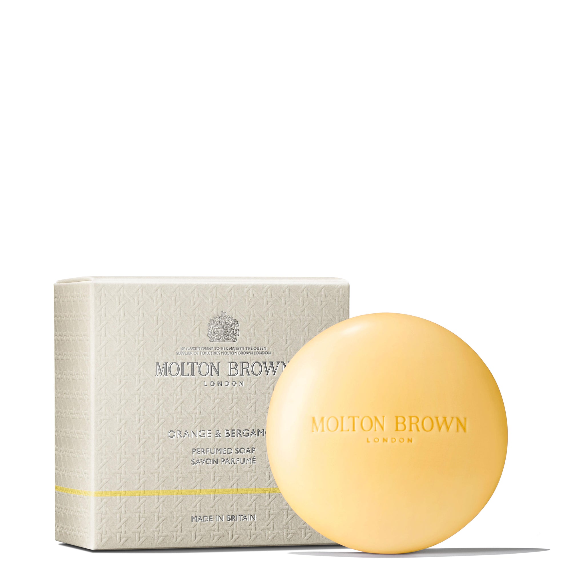 A round, orange Orange & Bergamot Perfumed Soap from Molton Brown Cyprus, exuding a citrus fragrance with hints of bergamot, is displayed in front of its textured beige box. The packaging features sophisticated branding and details like the words Molton Brown London and Made in Britain.