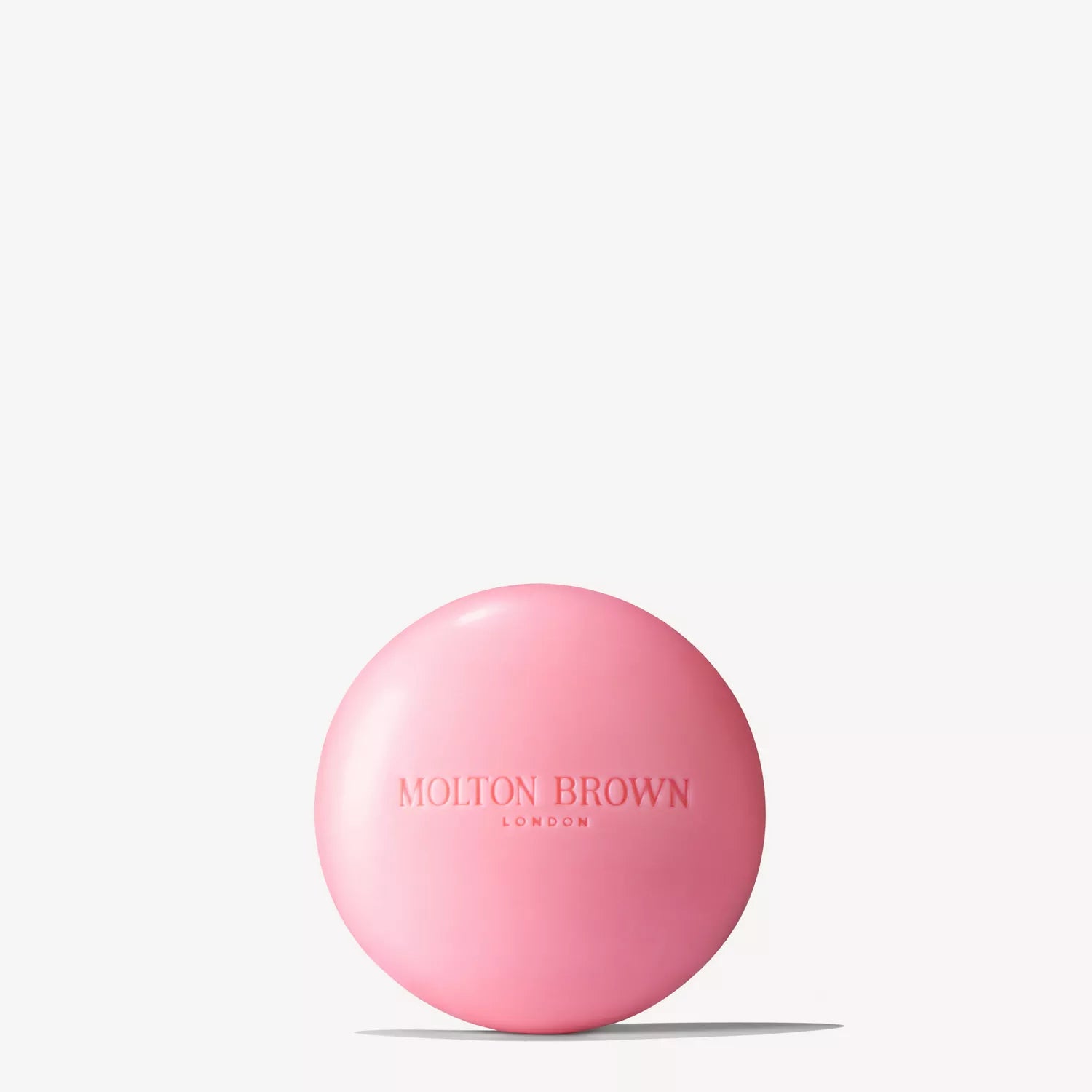 A circular pink soap with MoltonBrown Cyprus engraved on its surface emits a gentle woody-spicy scent of Fiery Pink Pepper, showcased against a simple white backdrop.