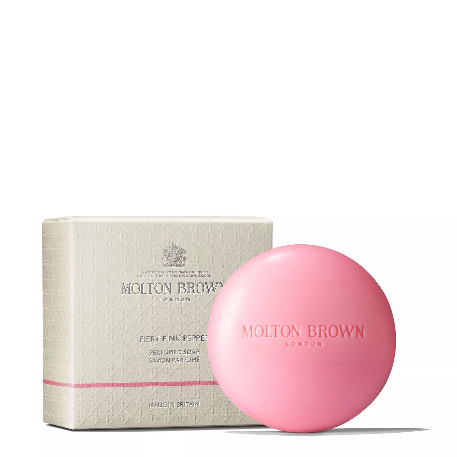 A pink circular soap from MoltonBrown Cyprus is placed next to its sophisticated cream-colored box, which features a textured design and Fiery Pink Pepper label. This woody-spicy soap, known as the Fiery Pink Pepper Perfumed Soap 150g, is enriched with shea butter for a luxurious experience.