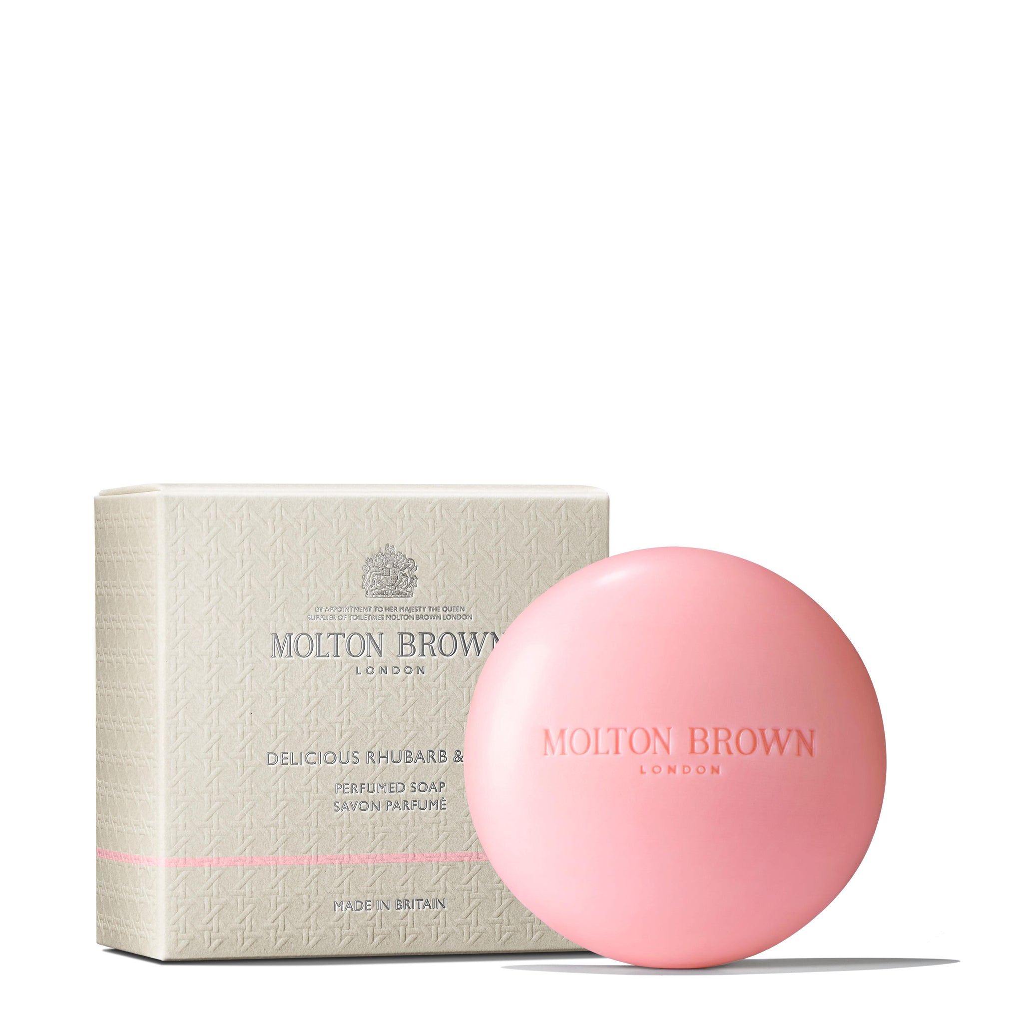 A round, pink soap labeled Rose Dunes Body Lotion 300ml from MoltonBrown Cyprus is positioned beside its matching beige box with a subtle pattern, exuding an ambery-rose scent. The soap has a smooth, glossy finish that promises delightful hydration.