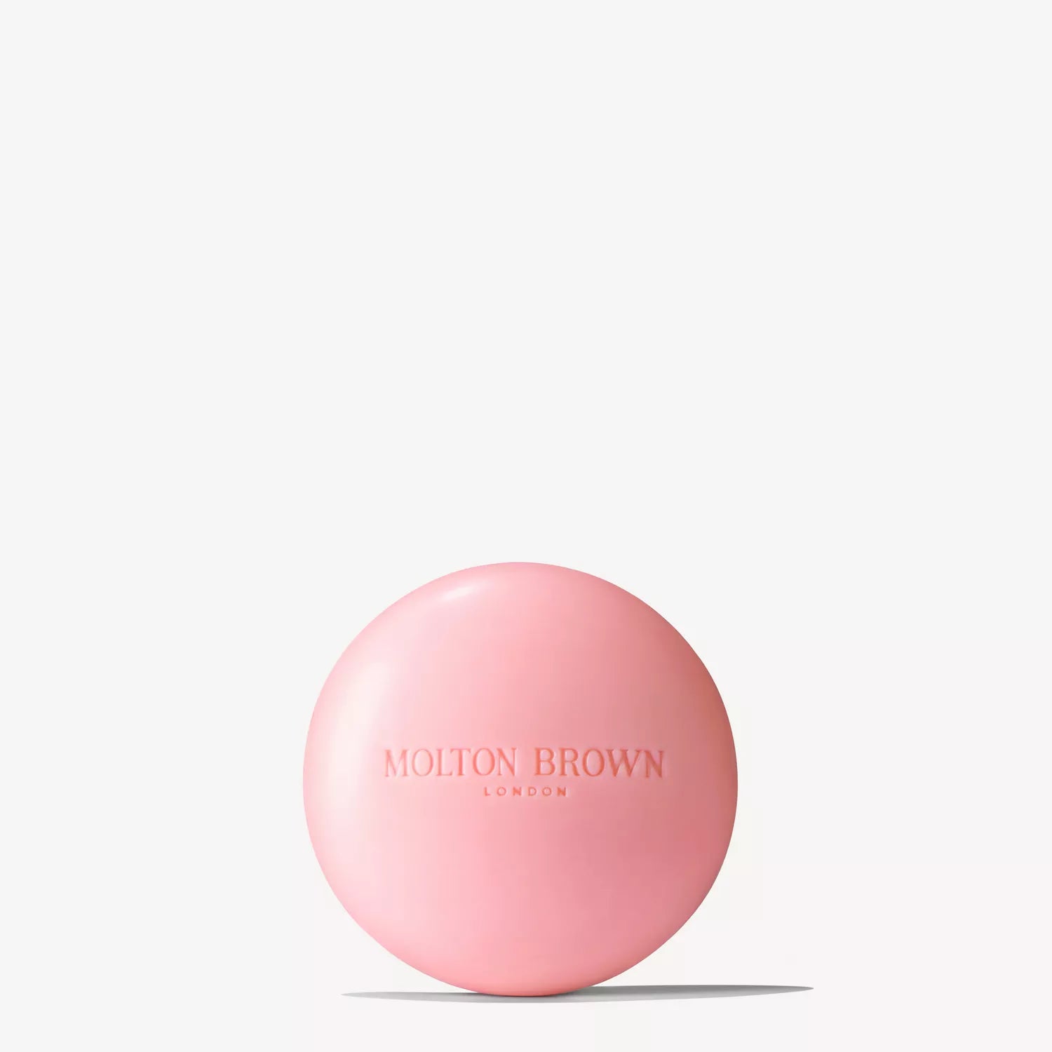 A round, pink Delicious Rhubarb & Rose Perfumed Soap bar embossed with Molton Brown Cyprus sits on a plain white background, exuding a floral-fruity scent and casting a faint shadow below.