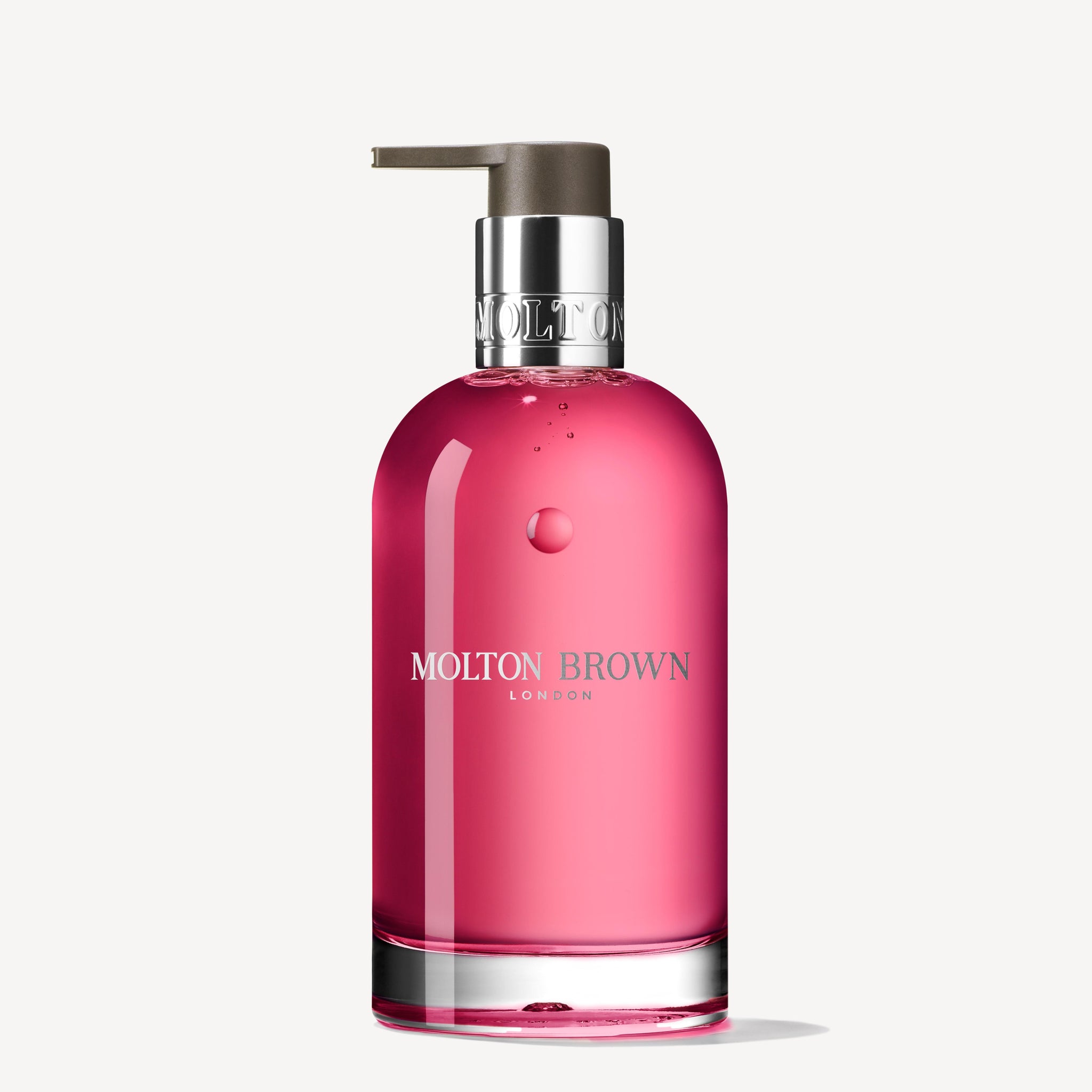 The Fiery Pink Pepper Fine Liquid Hand Wash by Molton Brown Cyprus is presented in a 200ml glass-like bottle with a silver pump. Its vibrant pink liquid exudes luxury, featuring the brand name and crest in white lettering on its elegant design.