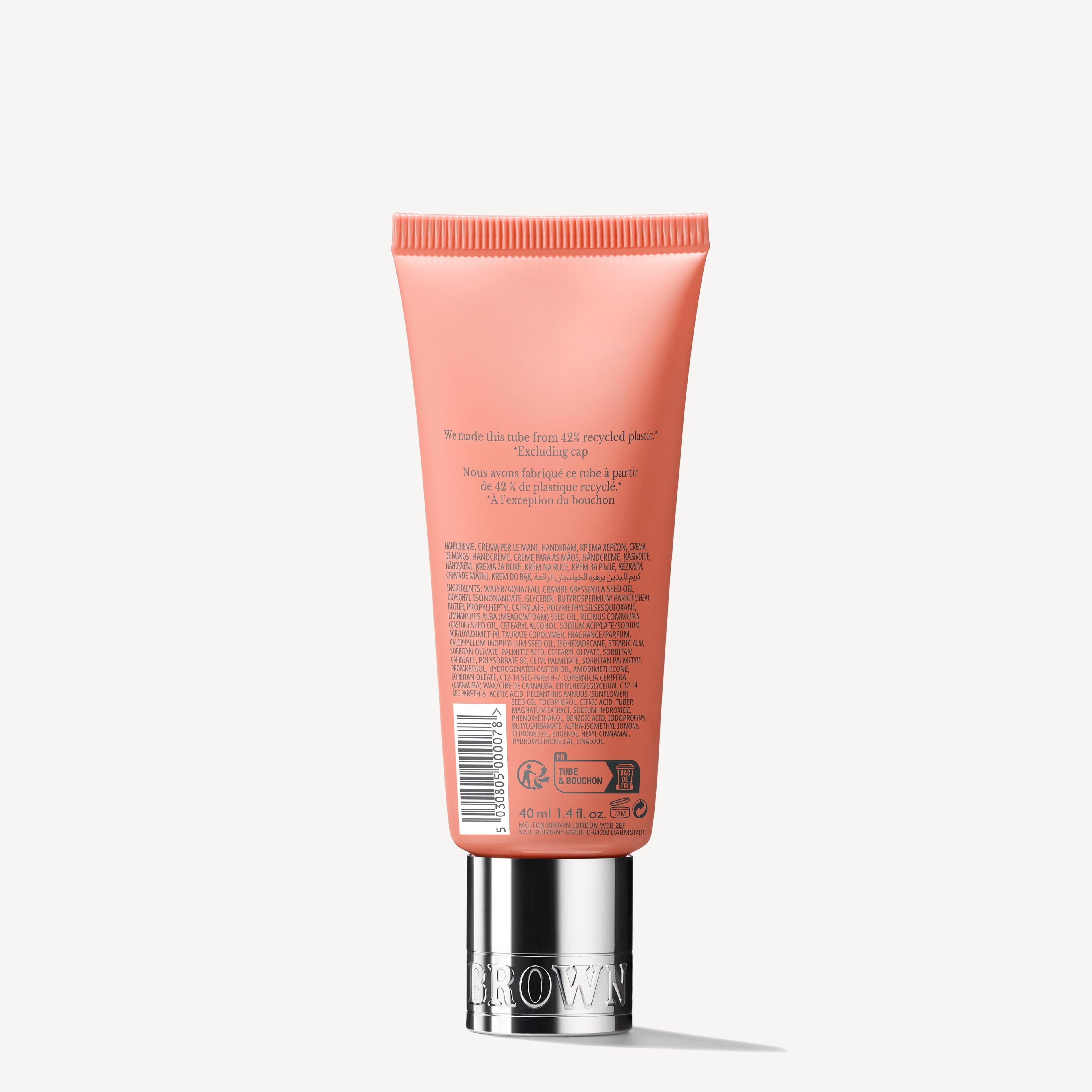 A coral-colored tube of MoltonBrown Cyprus's Heavenly Gingerlily Hand Cream, standing upright against a plain background, showcases silver accents on the cap and displays text indicating it's made from 57% recycled plastic. Fragranced for a pleasant experience, the back label features product information and recycling icons.