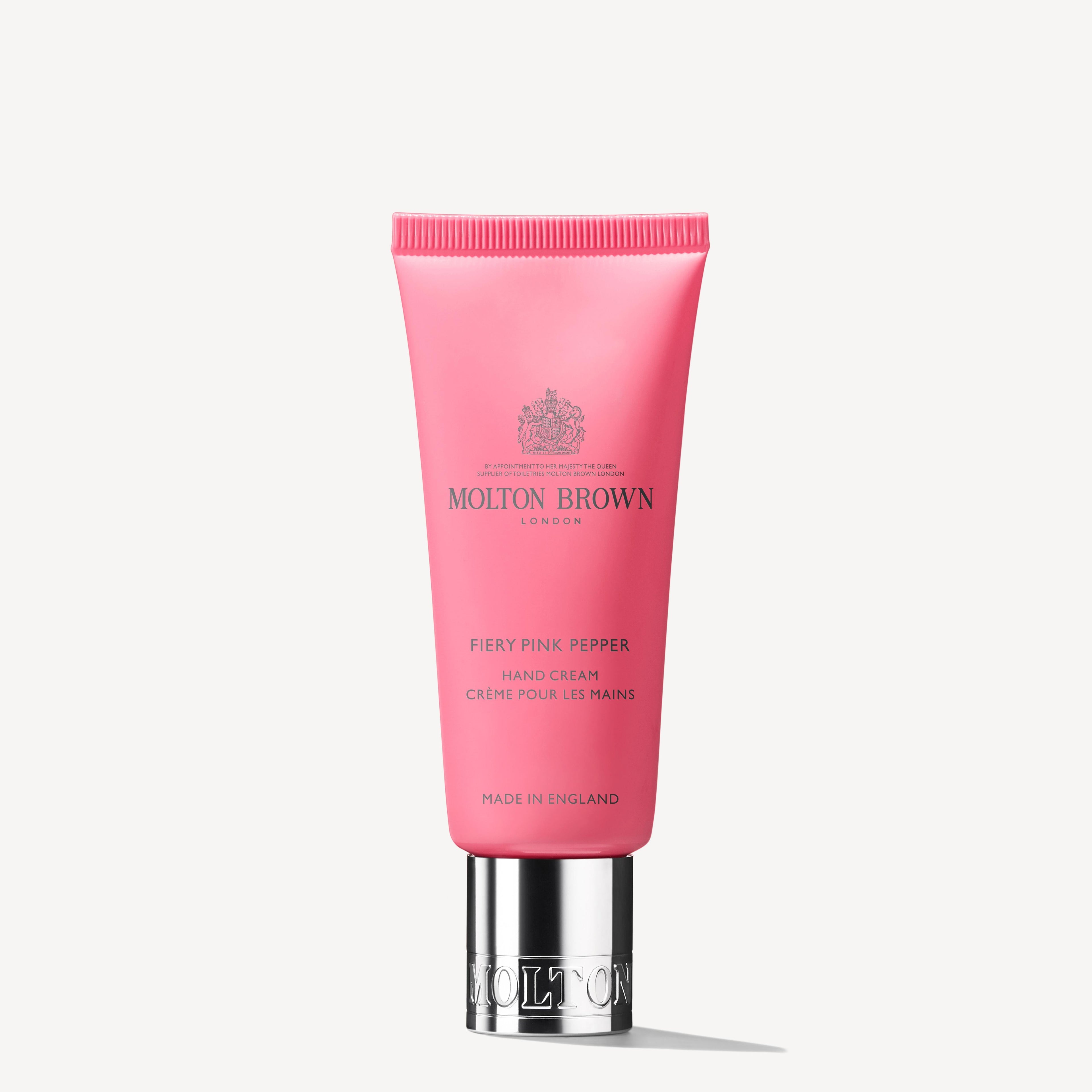 A 40ml pink tube of MoltonBrown Cyprus Fiery Pink Pepper Hand Cream, infused with ginger hints, features elegant silver lettering and a shiny silver cap, with "Made in England" proudly shown at the bottom.