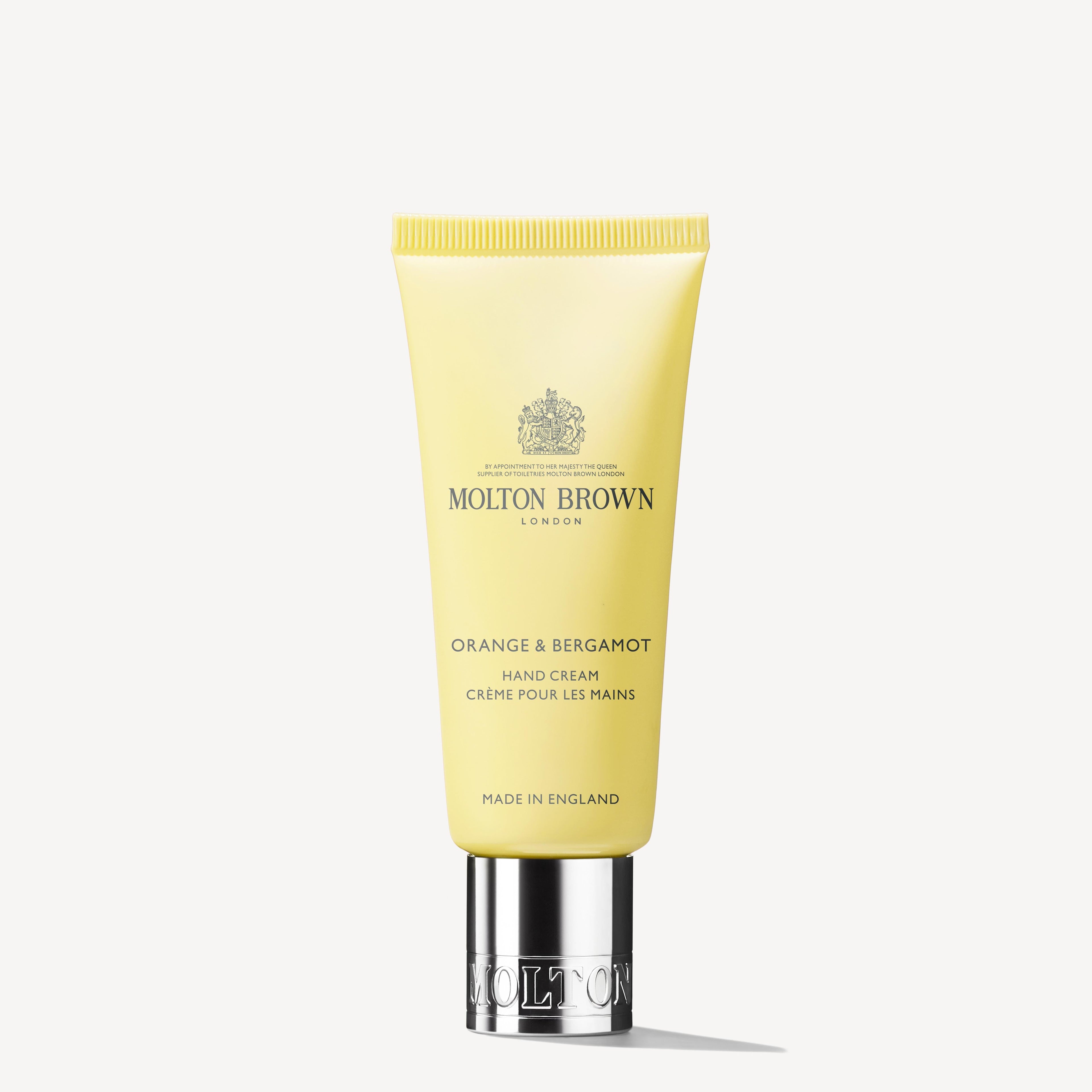 An Orange & Bergamot Hand Cream 40ml by MoltonBrown Cyprus, in a yellow tube with a silver cap, stands upright. The label features text and a crest logo that highlights hints of mandarin and neroli against a plain white background.