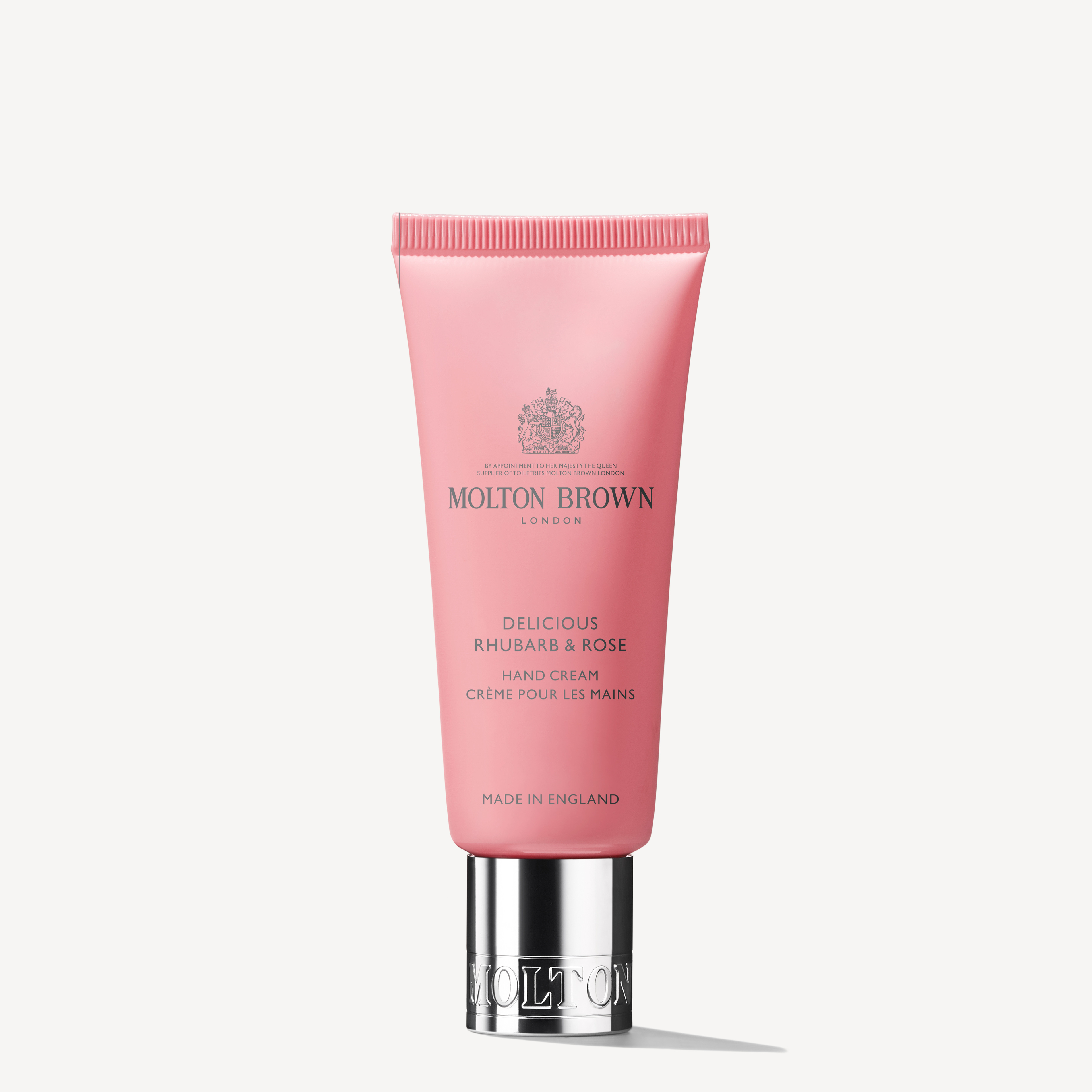 A pink tube of Delicious Rhubarb & Rose Hand Cream, by MoltonBrown Cyprus, is set against a plain white background. This moisturising gem, topped with a silver cap, features vibrant rhubarb leaf notes and proudly displays 'Made in England' at the bottom.