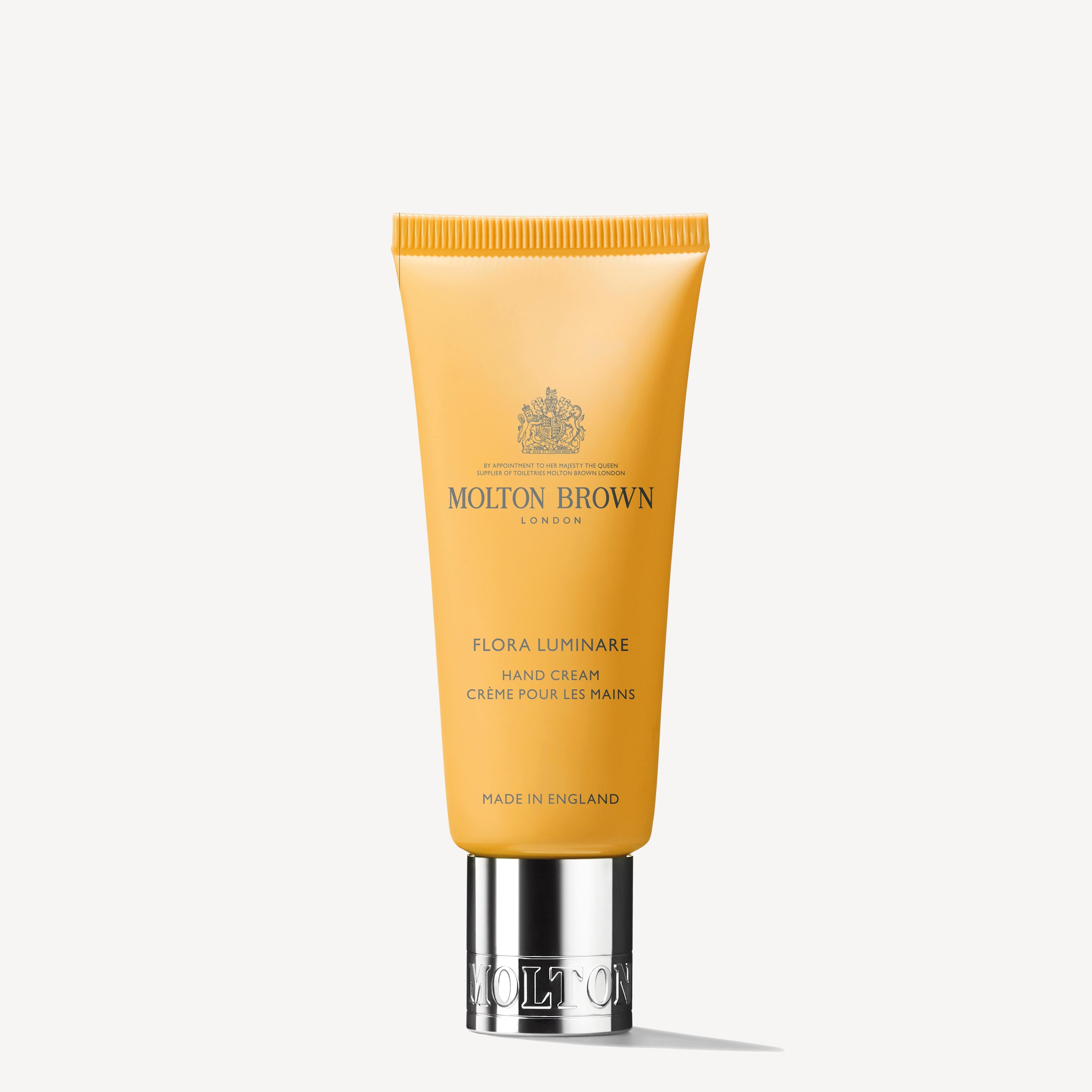 A yellow tube of Flora Luminare Hand Cream by MoltonBrown Cyprus, featuring solar notes and a silver cap, prominently displays the brand's logo and text in black. Crafted in England, this luxurious 40ml formula provides rich hydration.