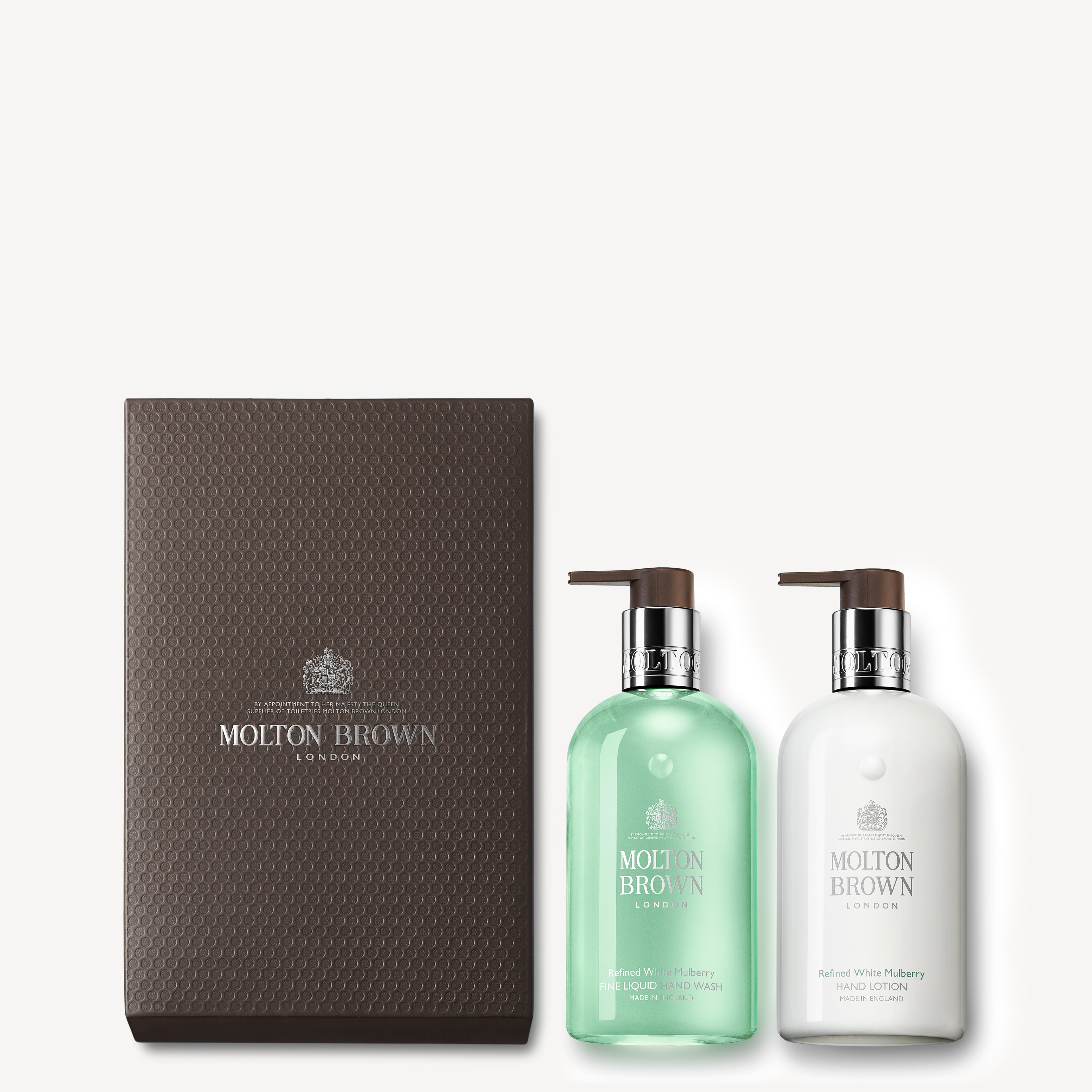 Introducing the Refined White Mulberry Hand Wash & Lotion Set by MoltonBrown Cyprus: This elegant gift set includes two pump dispenser bottles—a herbaceous hand wash infused with clary sage fragrance and a white lotion. They are beautifully presented alongside a textured brown box featuring the Molton Brown logo.