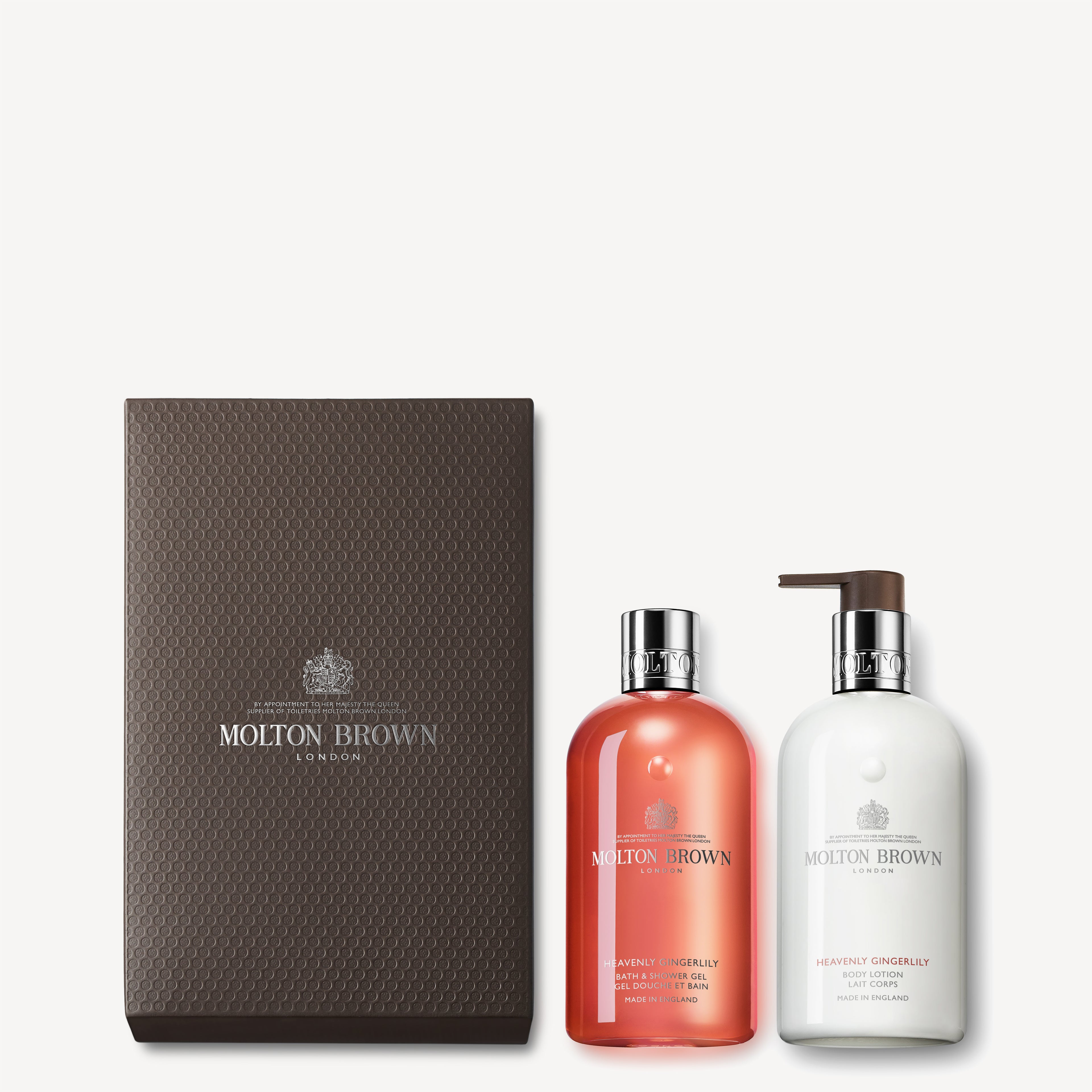 Introducing the Heavenly Gingerlily Shower Gel & Lotion Gift Set by Molton Brown Cyprus, which includes two exquisite bottles: a vibrant orange Fiery Pink Pepper Bath & Shower Gel and a pristine white Heavenly Gingerlily Body Lotion. These luxurious items are gracefully displayed alongside a textured brown box embellished with the Molton Brown logo.