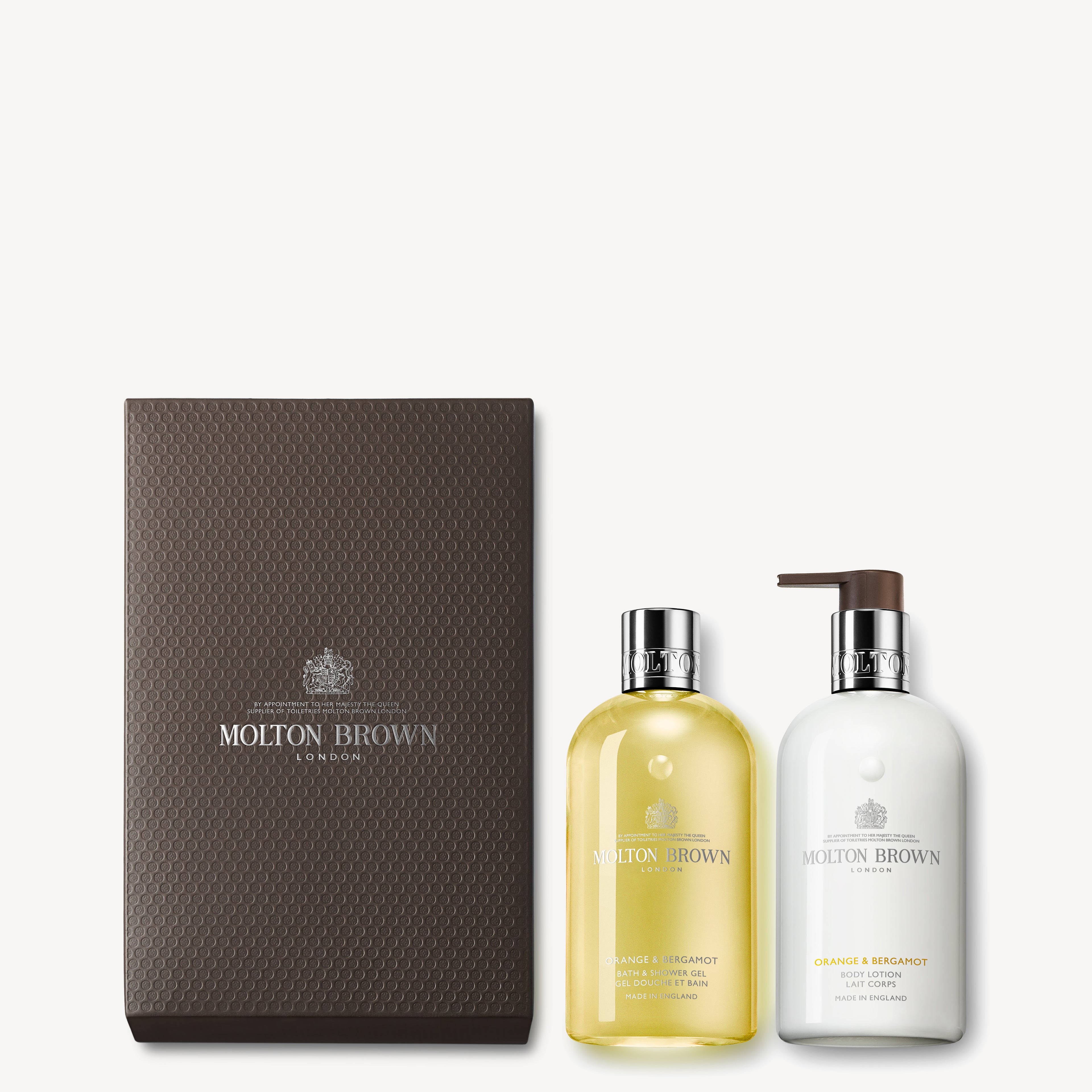 The Orange & Bergamot Shower Gel & Lotion Gift Set from MoltonBrown Cyprus features a vibrant yellow shower gel and a luxurious body lotion, both infused with the signature Orange & Bergamot scent. They are elegantly displayed beside a textured brown box adorned with the MoltonBrown logo.