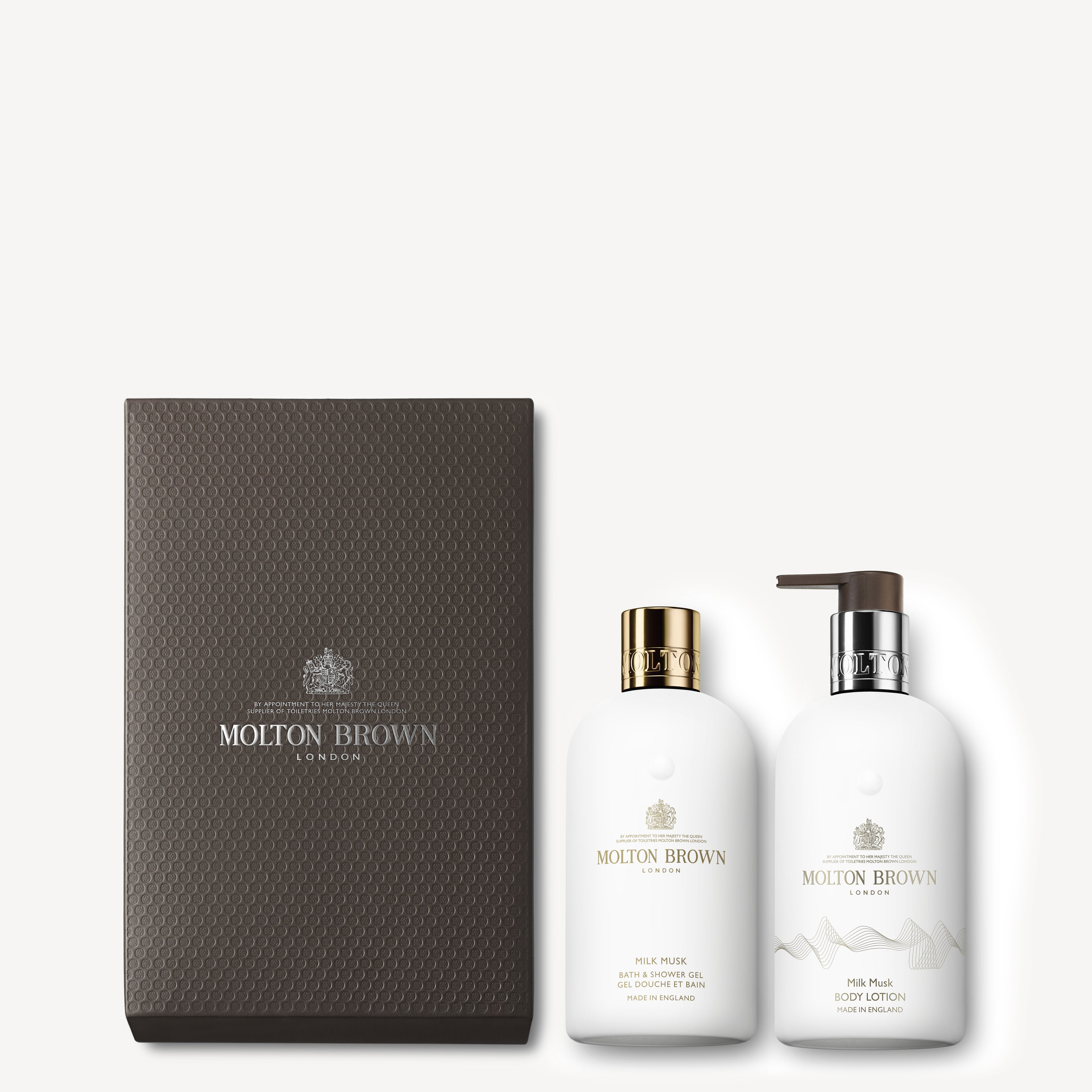 A MoltonBrown Cyprus Milk Musk Gift Set presented in a dark textured box includes two elegantly designed white bottles: one containing bath and shower gel with a gold cap, and the other featuring a body lotion with a convenient pump. Both items showcase the Molton Brown logo in refined typography—an exclusive treat for Bath & Body enthusiasts.