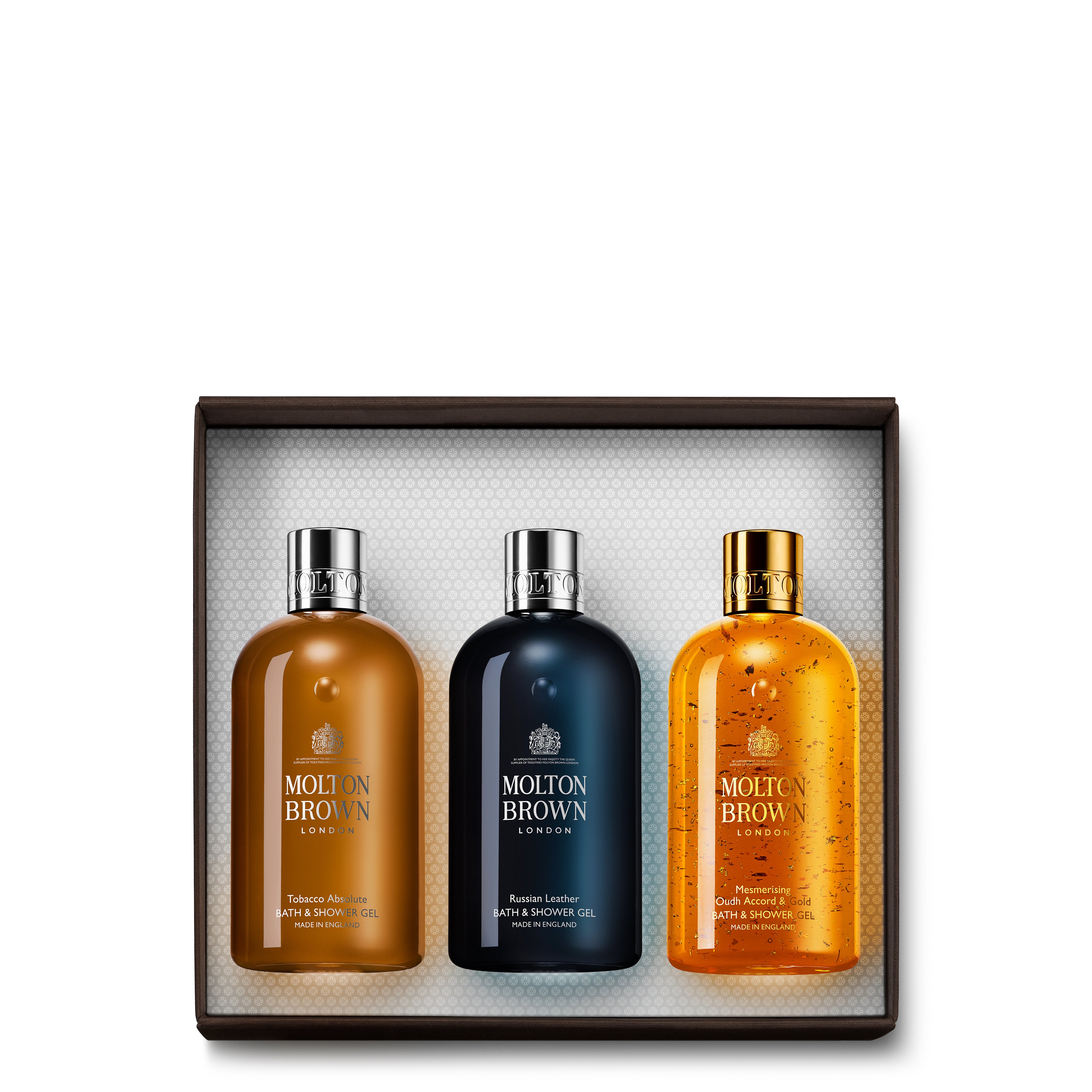 Introducing the Woody Gift Set by MoltonBrown Cyprus: a lavish collection of three woody Bath & Shower Gels, elegantly displayed in a presentation box. The amber, dark blue, and orange bottles feature silver caps and release opulent fragrances. Inside, the white textured interior enhances the set's sophisticated charm.