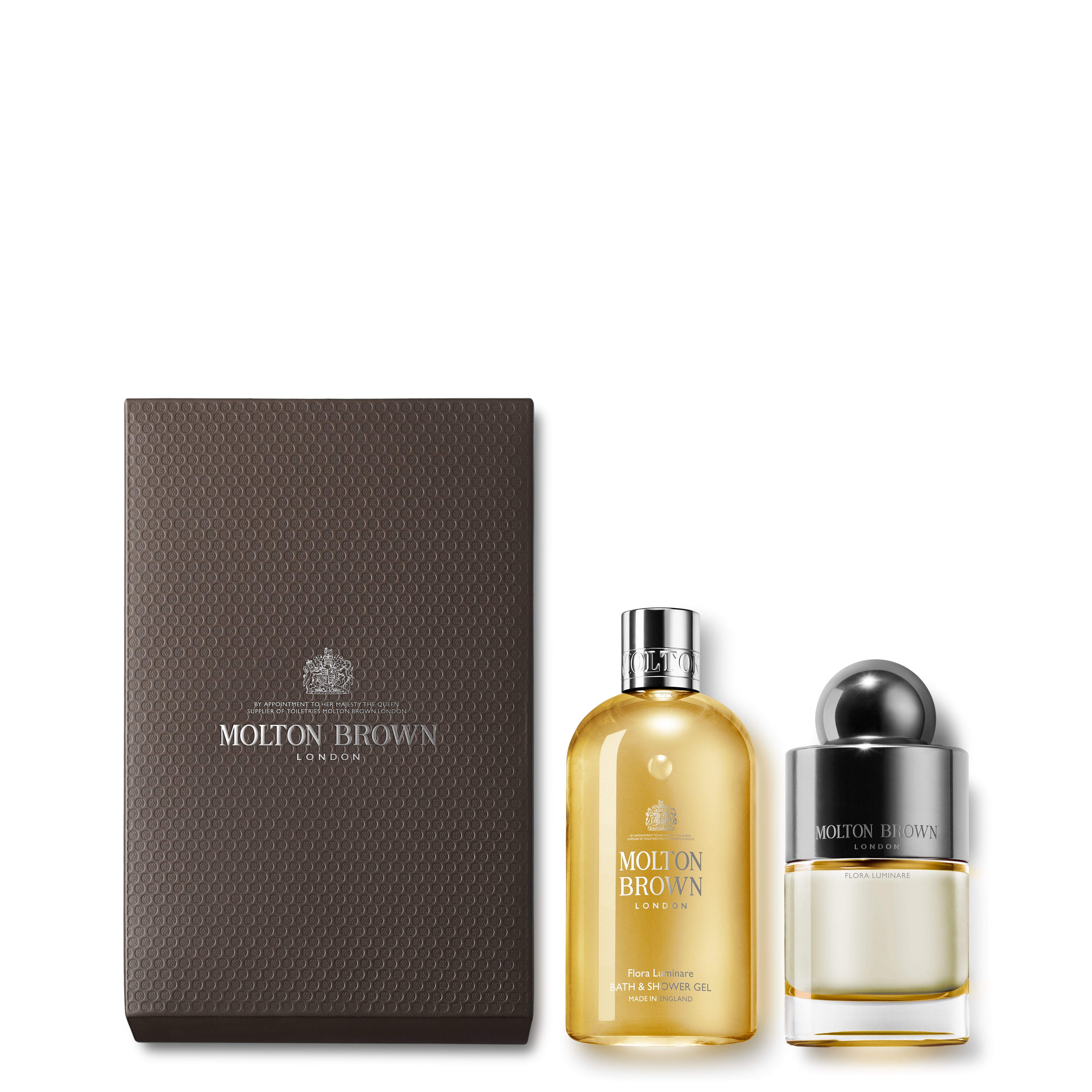 The 100ml Flora Luminare Fragrance Gift Set by MoltonBrown Cyprus features a textured brown box adorned with the brand logo, containing a tall golden bath and shower gel along with a shorter Eau de Toilette bottle showcasing a sleek black cap and white-floral fragrance.